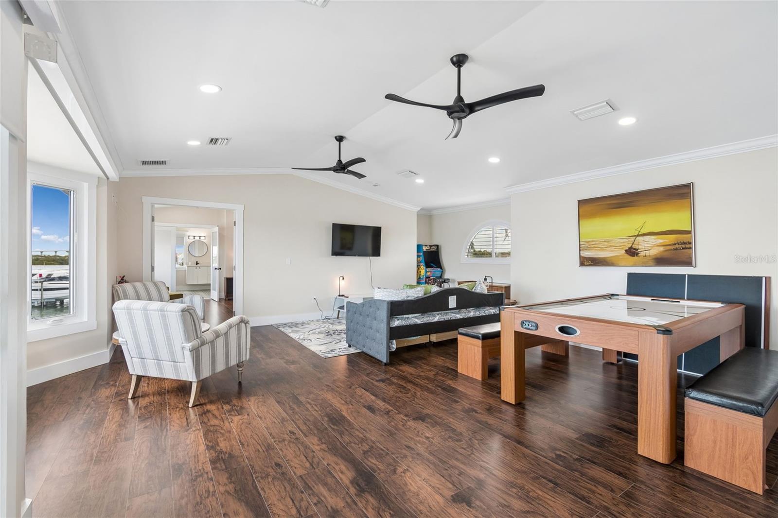 Furnished recreation room with a large game table, daybed, arcade game, and water visible through the window.