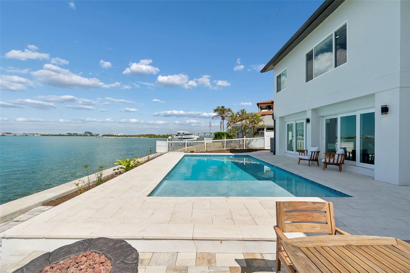 Waterfront home with a rectangular pool and stone patio beside the bay.