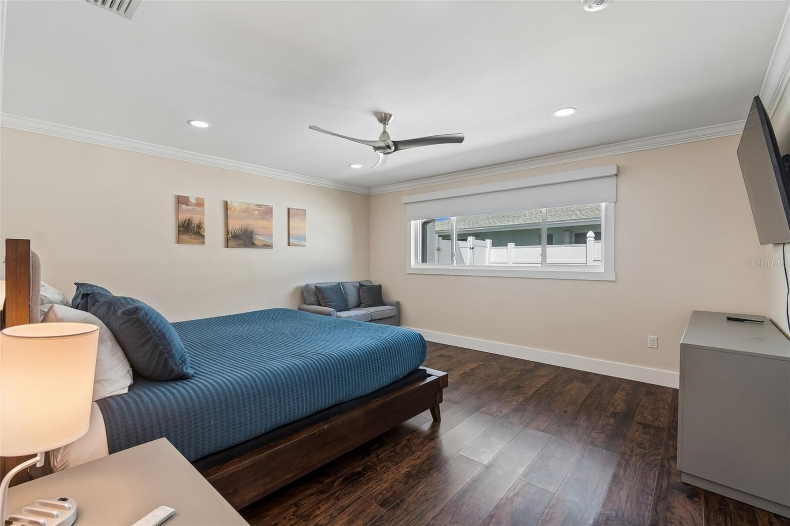Bedroom with a blue-covered bed, dark wood floors, and a wide horizontal window.