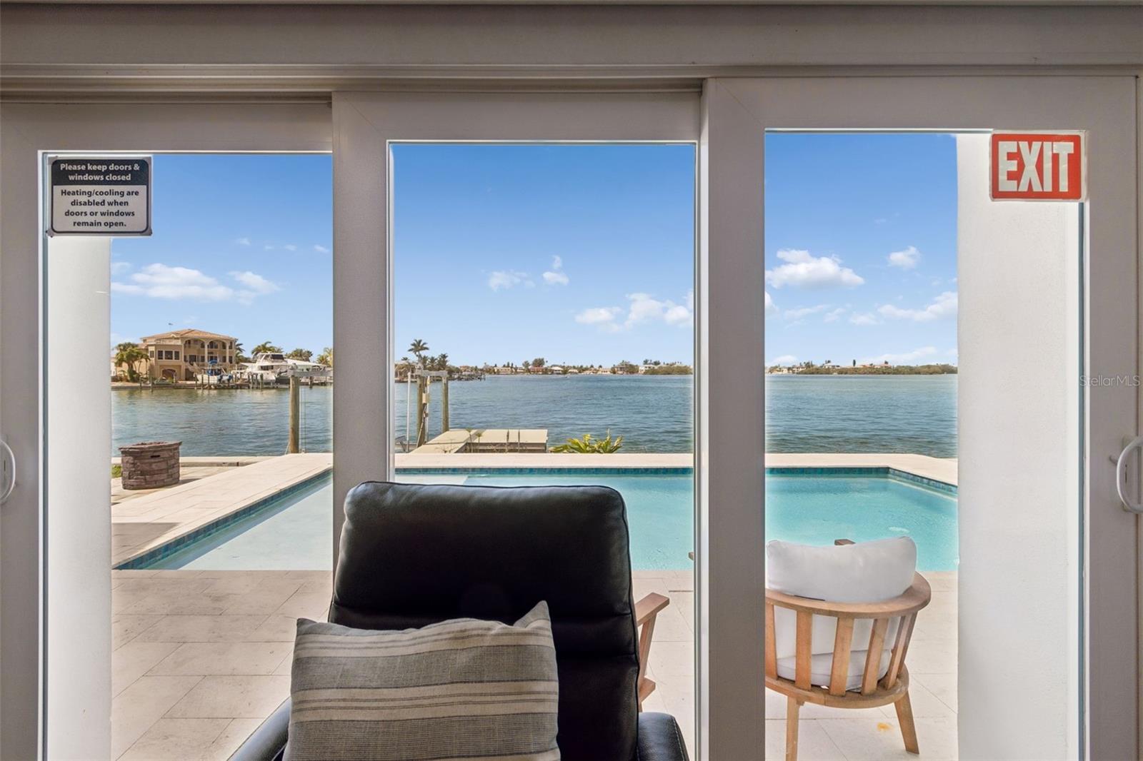 Living room opens through glass doors to a waterfront pool and bay.