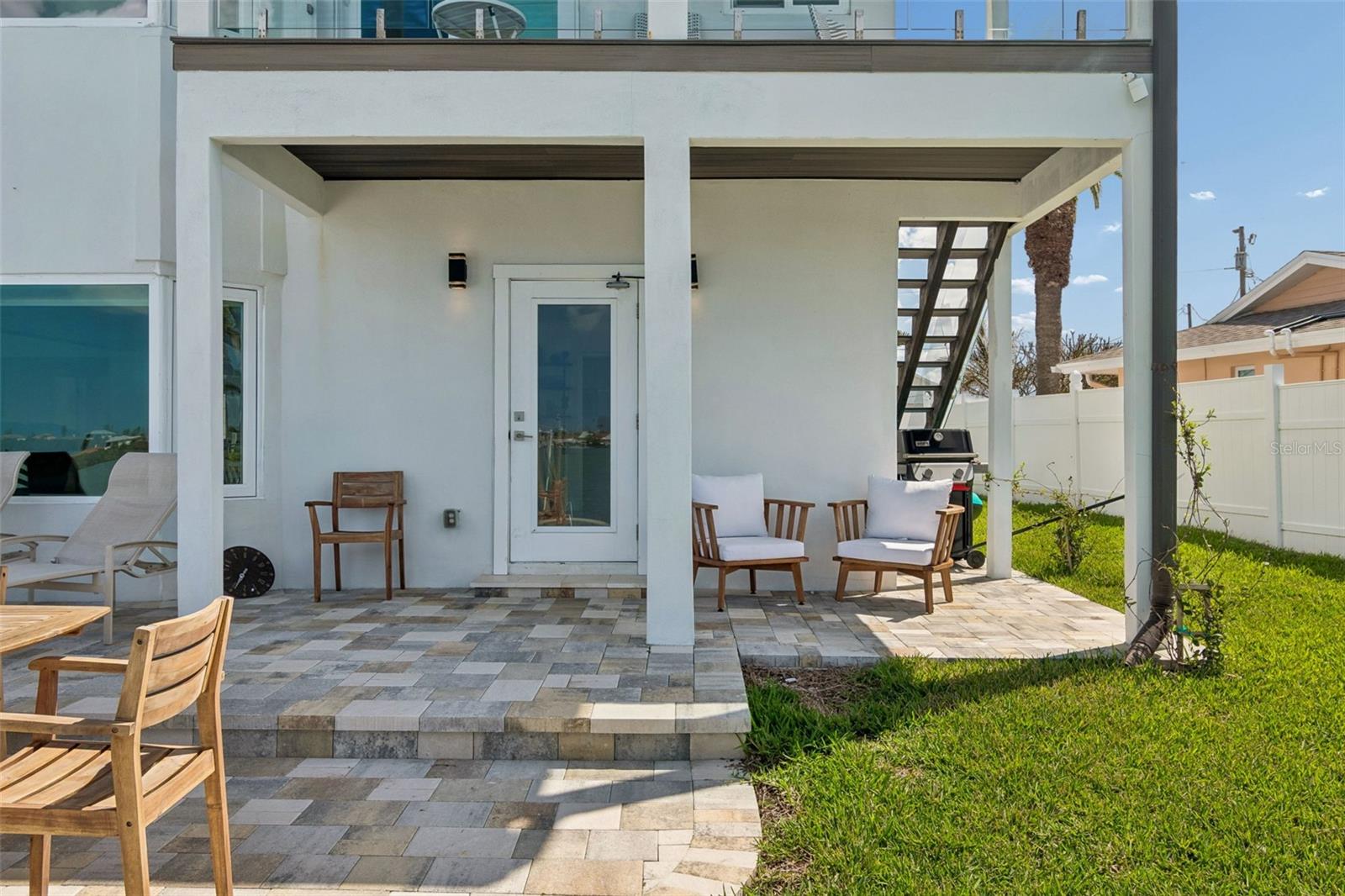 Covered patio with stone paving, wooden seating, an outdoor grill, and stairs to the upper deck.