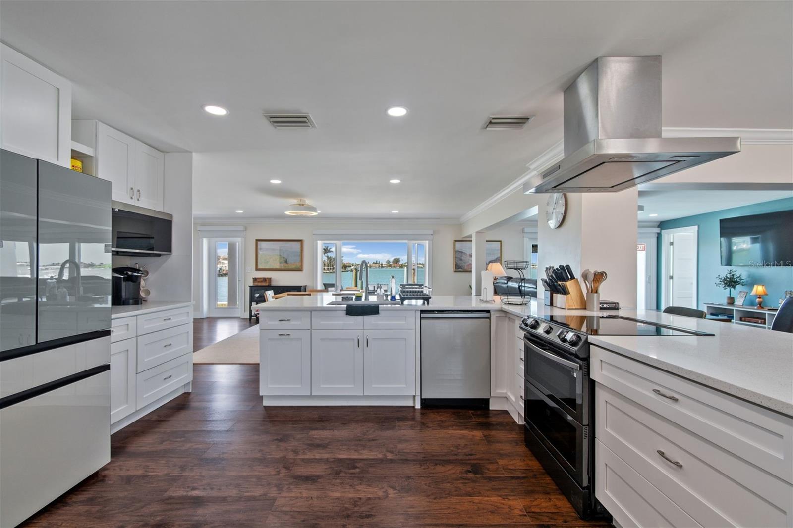 Bright white kitchen with a central island, stainless steel appliances, and water views through the windows.