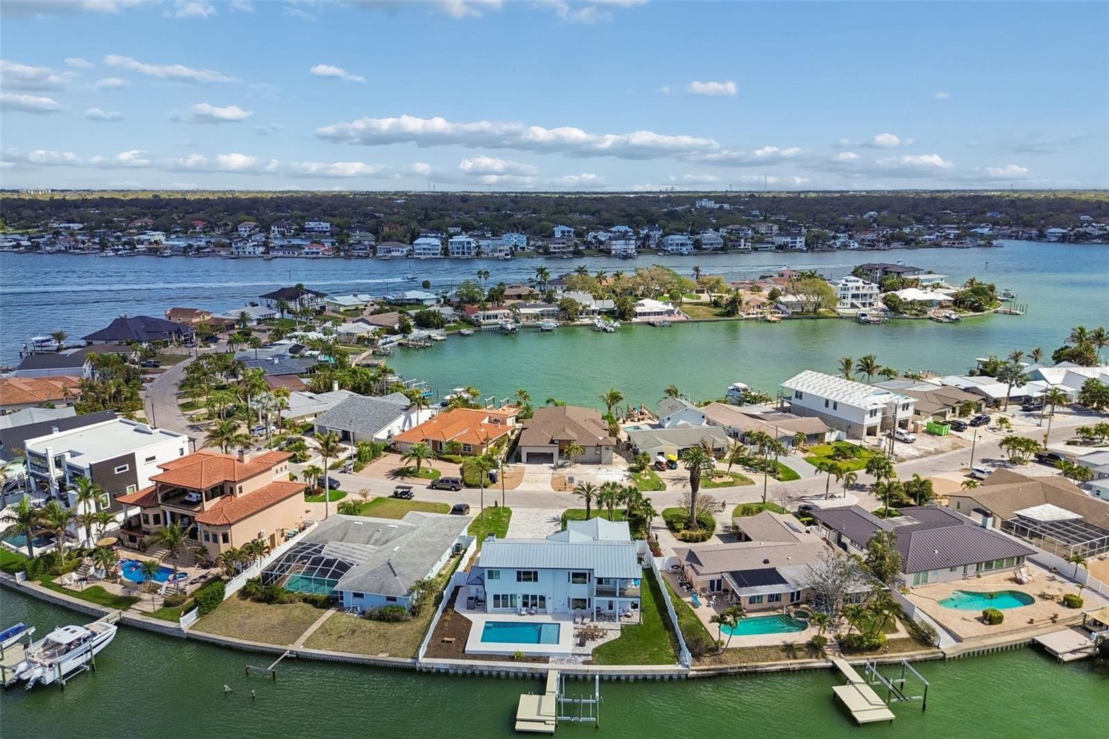 Aerial view of a waterfront home with a pool and dock, surrounded by canal-side houses.