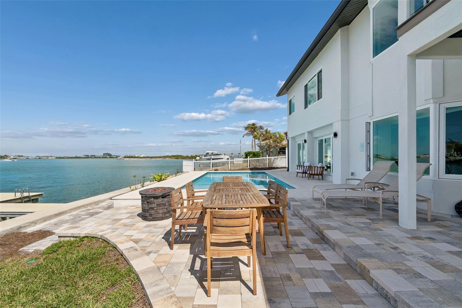 Waterfront pool patio with a wooden dining set and views across the bay.