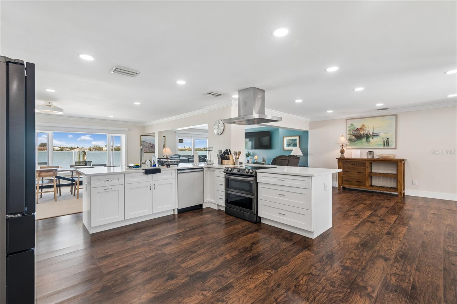 Open kitchen with a white island, dark wood floors, and a waterfront view through glass doors.
