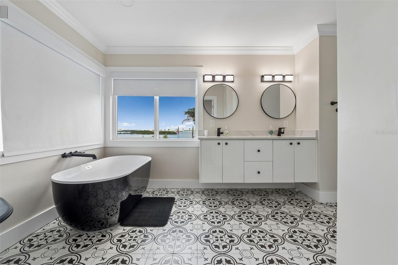 Bathroom with a freestanding patterned tub, ornate tile floor, and water visible through the window.