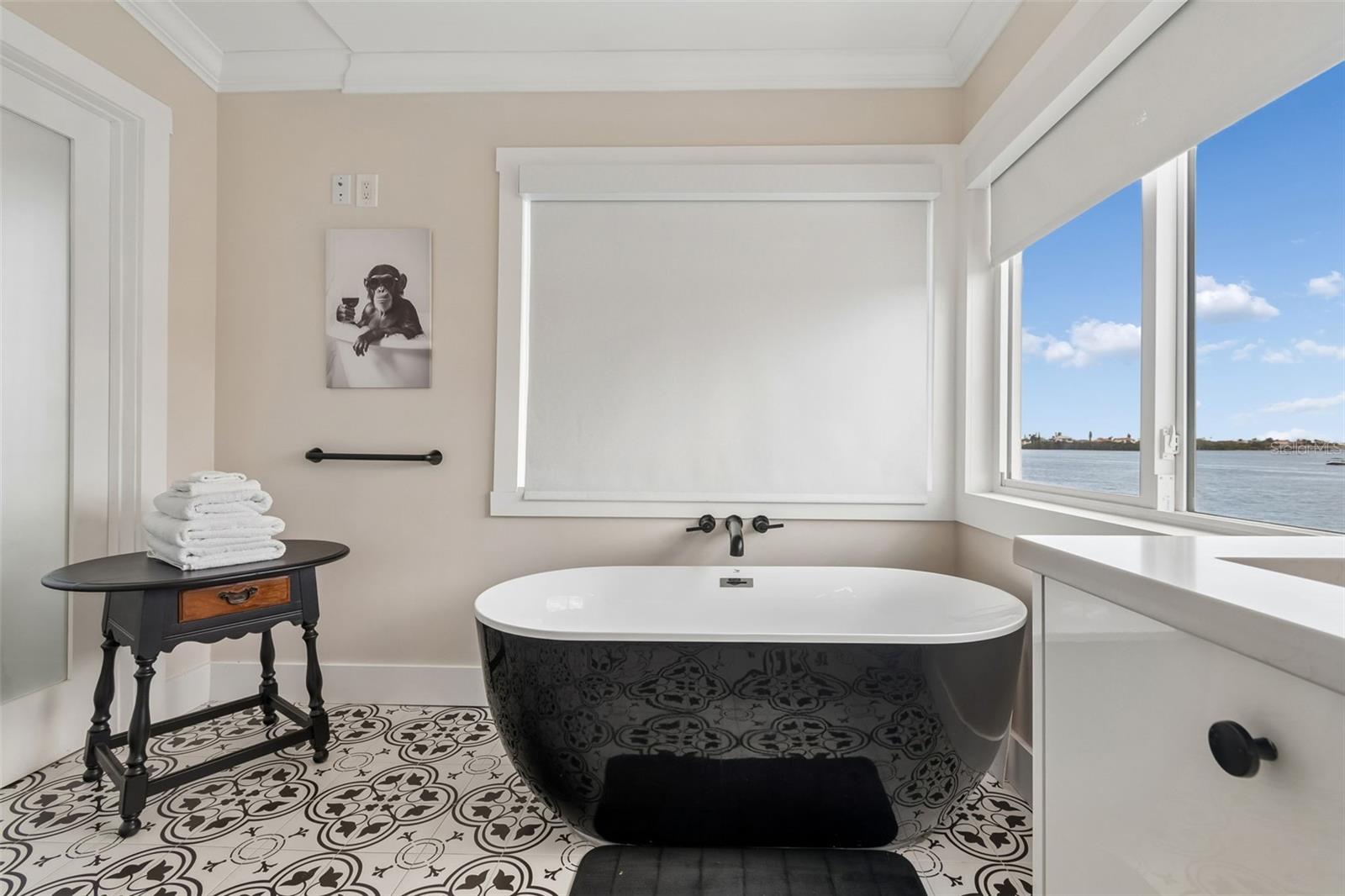 Bathroom with a freestanding black tub, patterned tile floor, and water view.