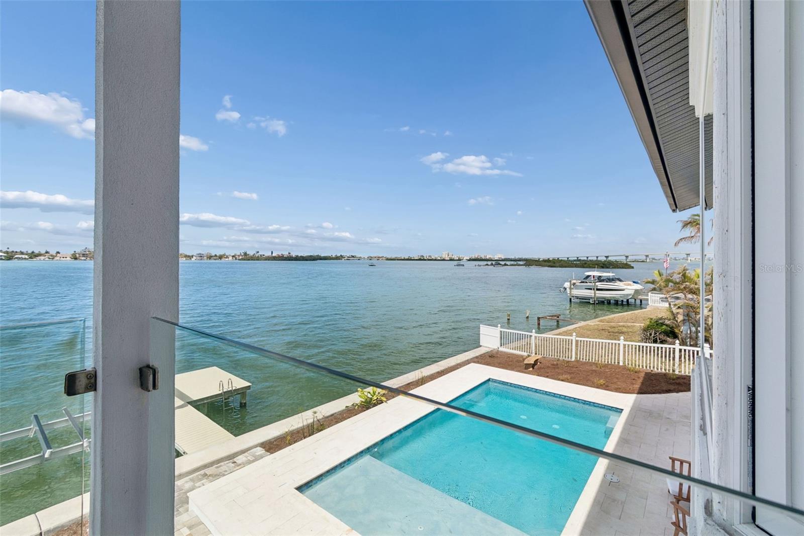 Waterfront pool and private dock overlook the bay from a glass-railed balcony.