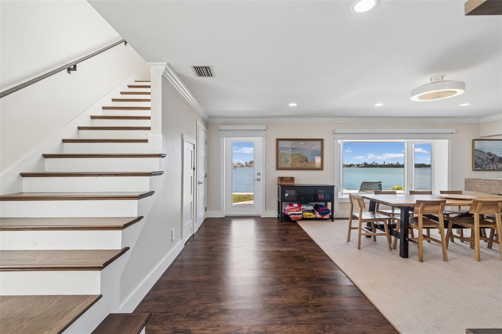 Dining area with a staircase and large windows overlooking the water.