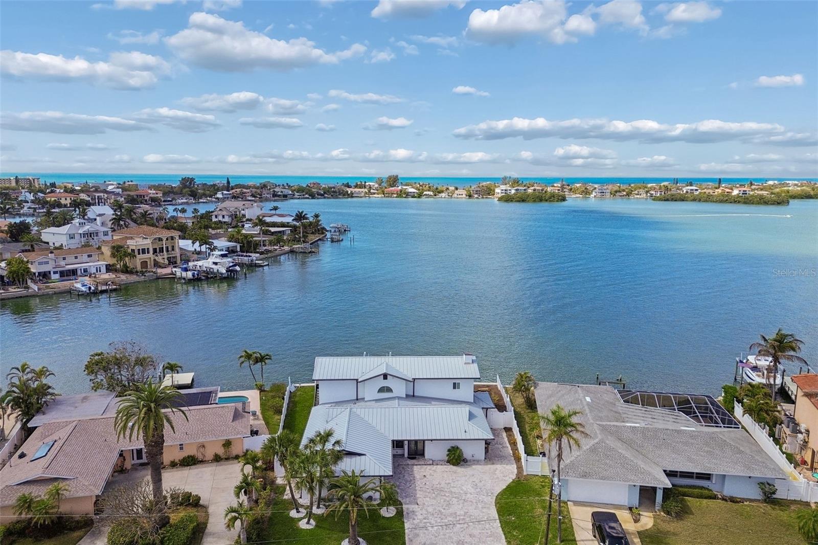 Aerial view of a waterfront home beside a broad bay, with the Gulf horizon beyond.