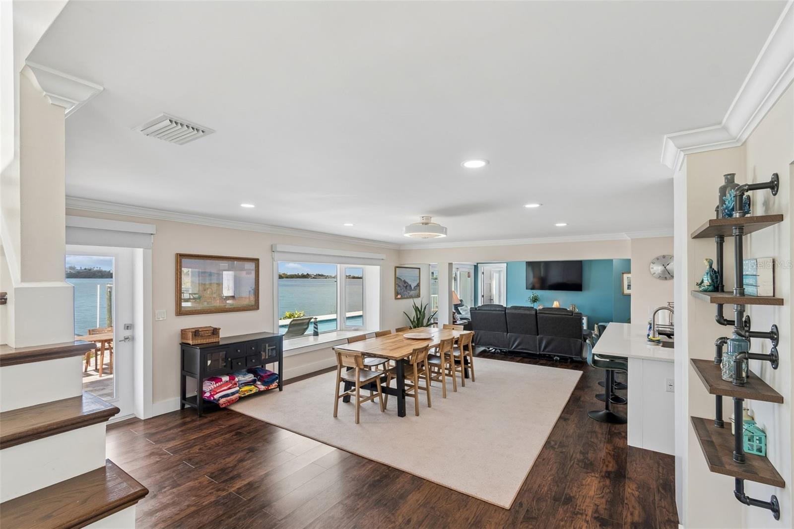 Open-plan living and dining room with water views through large windows and doors.