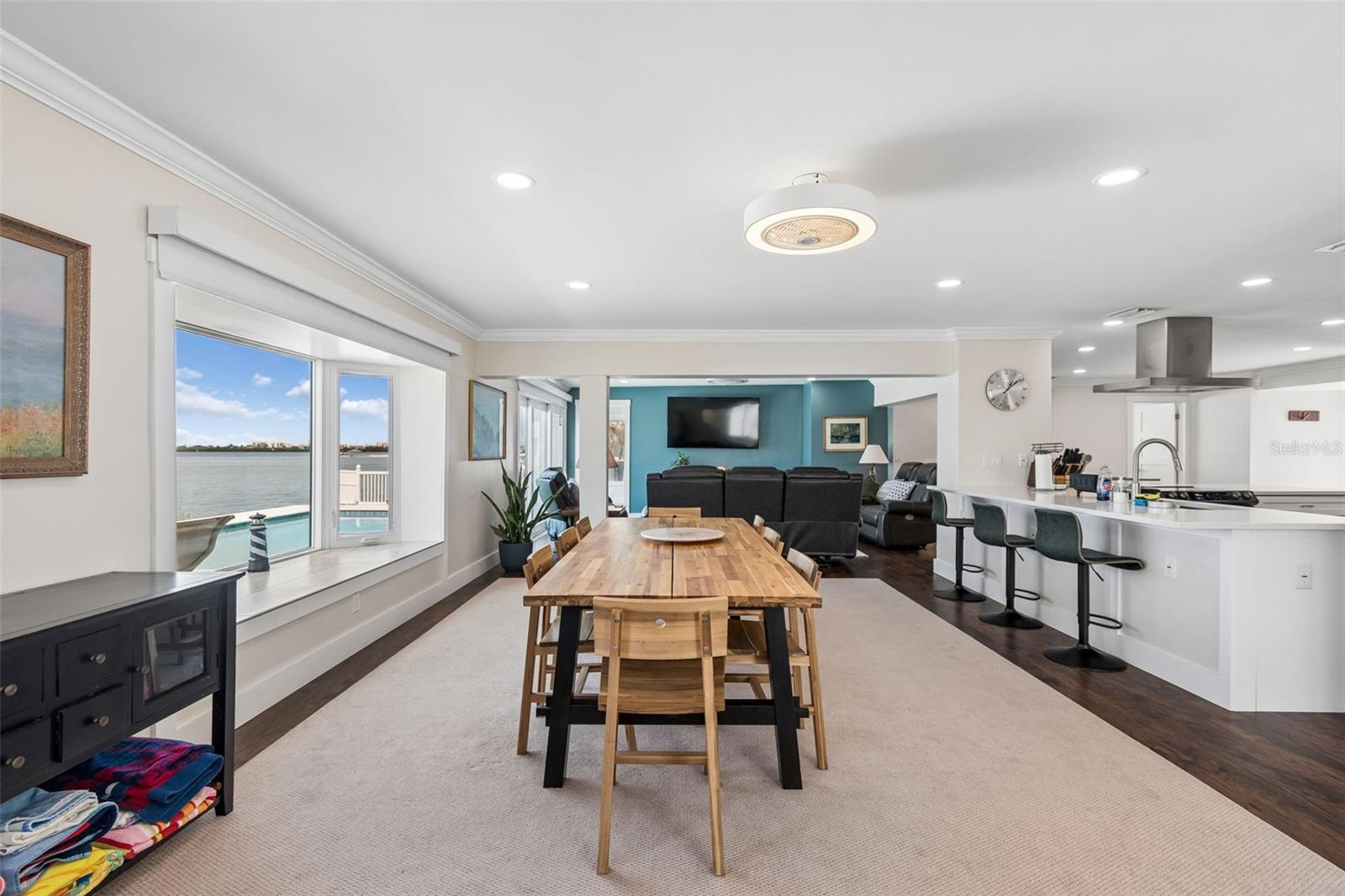 Open-plan dining room with a long wood table and water views through large windows.