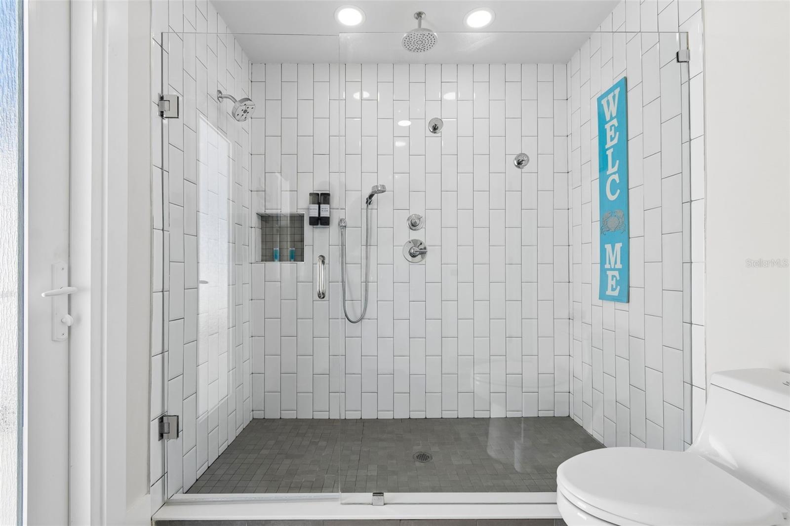 Bathroom with a spacious white-tiled walk-in shower, glass enclosure, and multiple showerheads.
