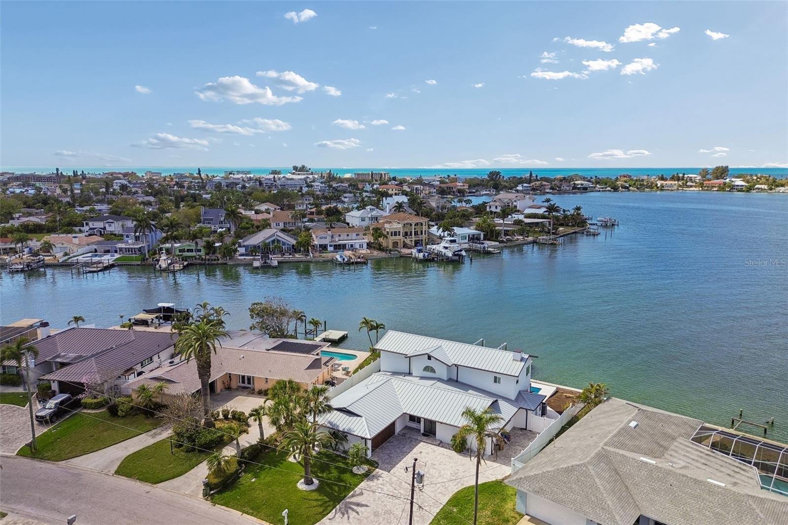 Aerial view of waterfront homes and docks along a bay, with the Gulf visible beyond.