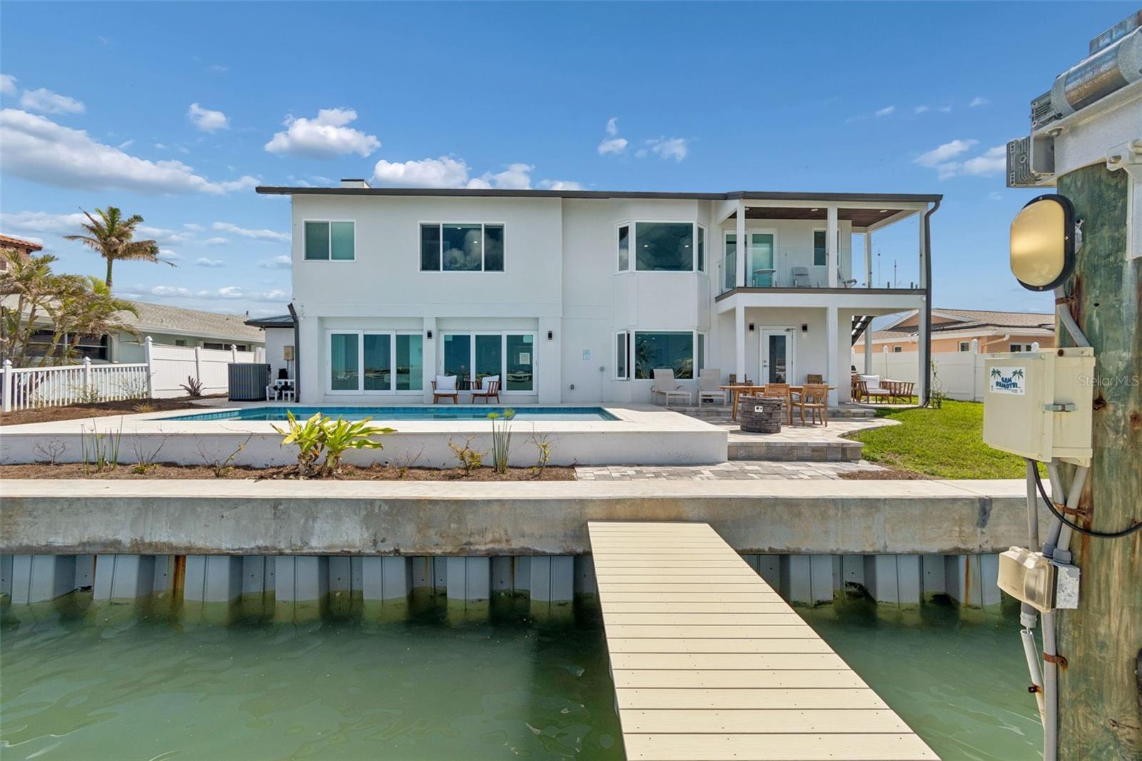 Waterfront home with a pool, covered balcony, and dock extending into the canal.