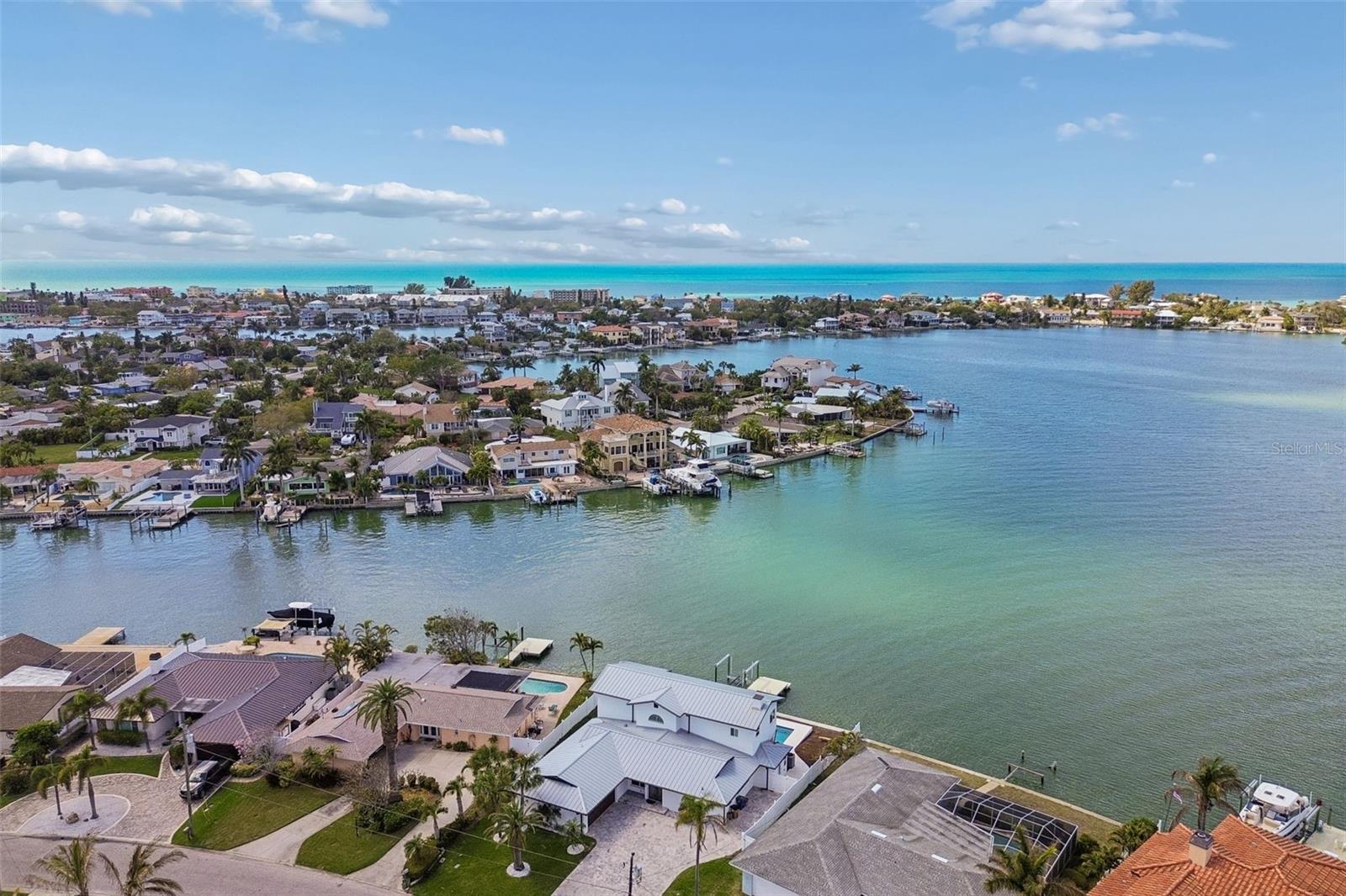 Aerial view of waterfront homes and docks beside a bay, with the Gulf of Mexico on the horizon.