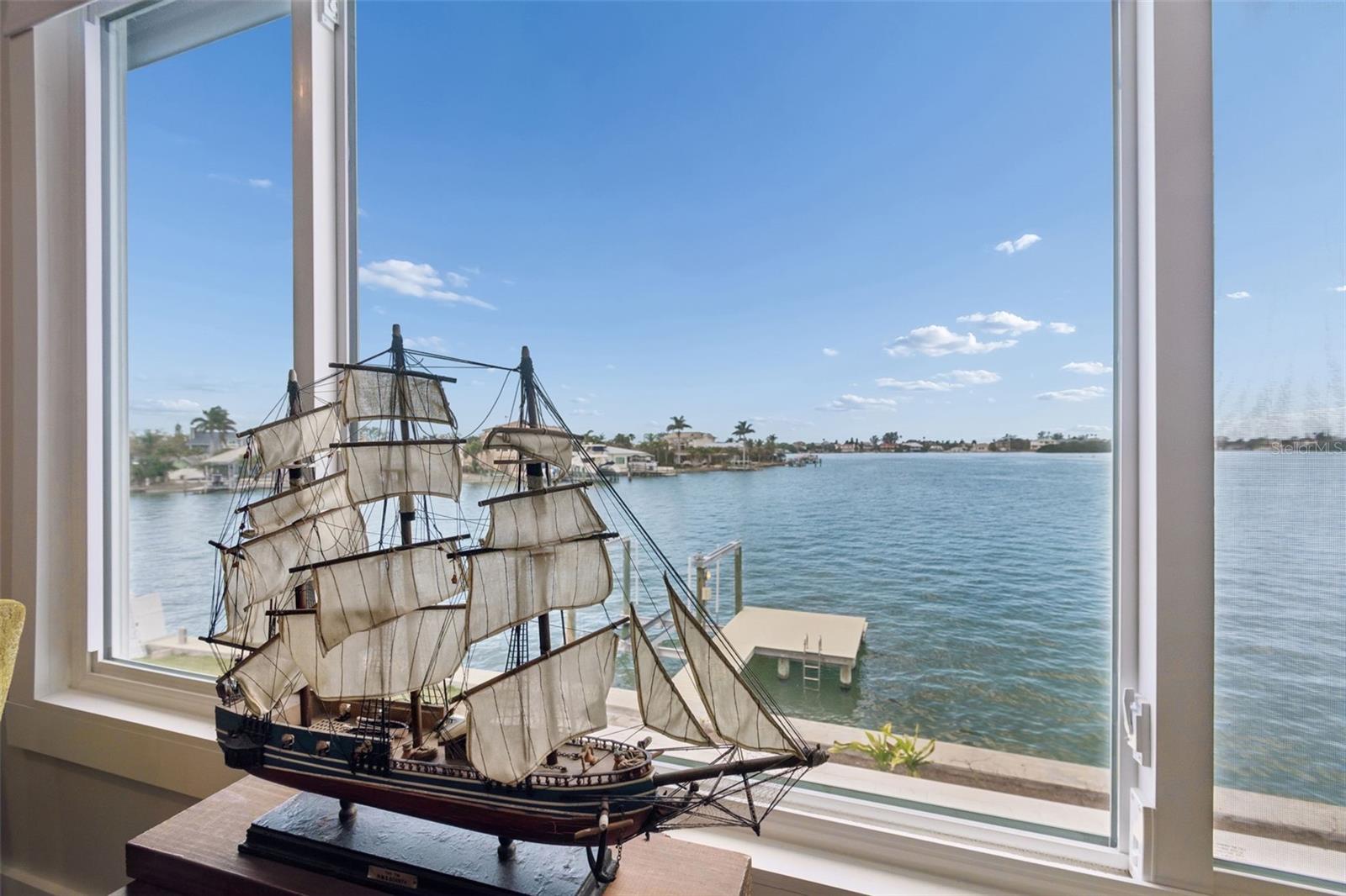 Waterfront view through a large window, with a model sailing ship in the foreground.