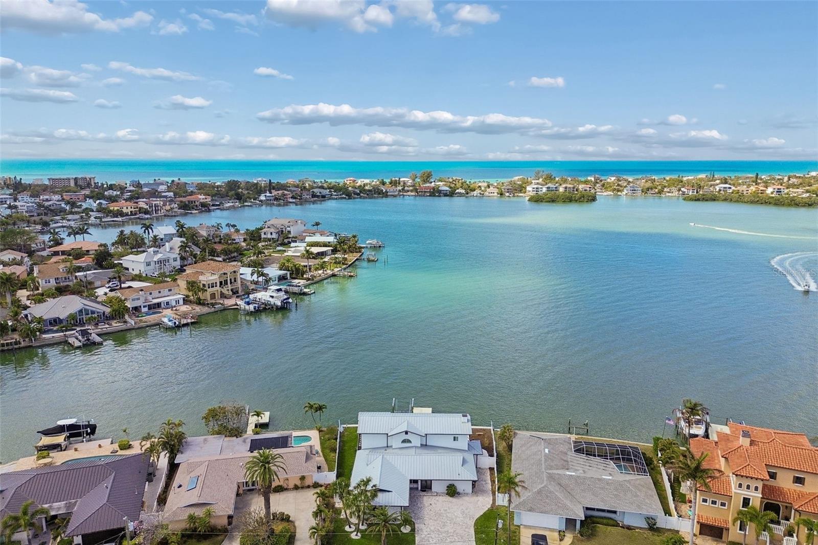 Aerial view of waterfront homes, a broad blue bay, and the Gulf horizon.