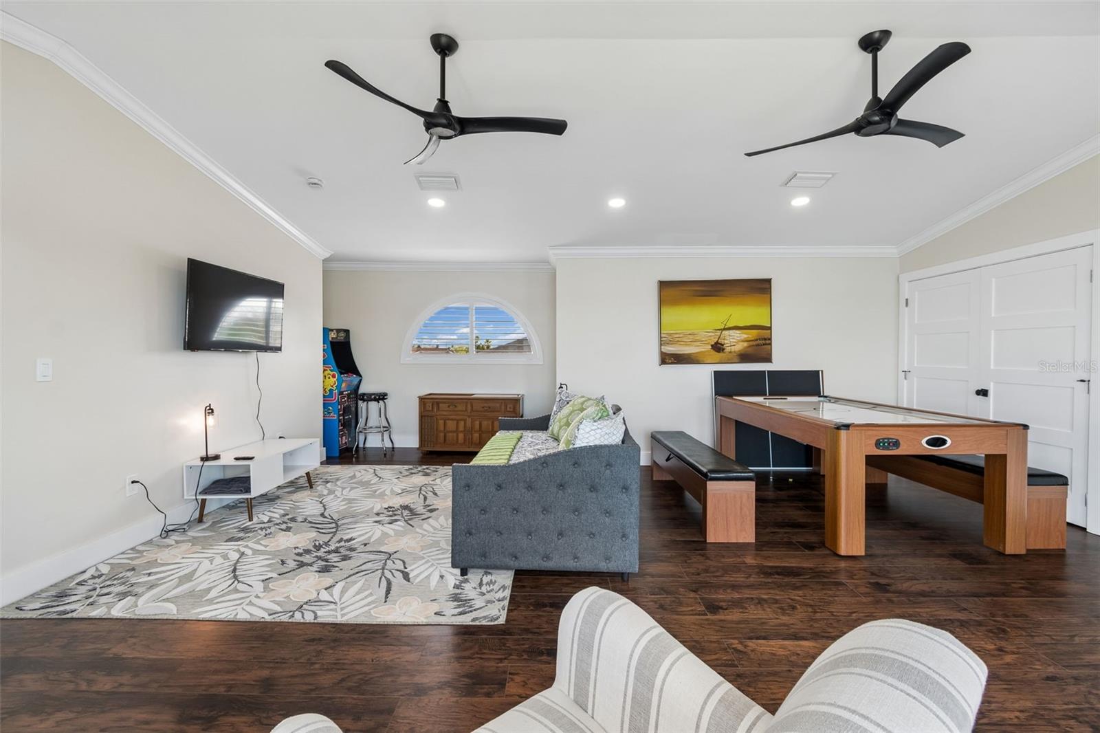 Furnished recreation room with a pool table, gray sofa, arcade game, and two ceiling fans.