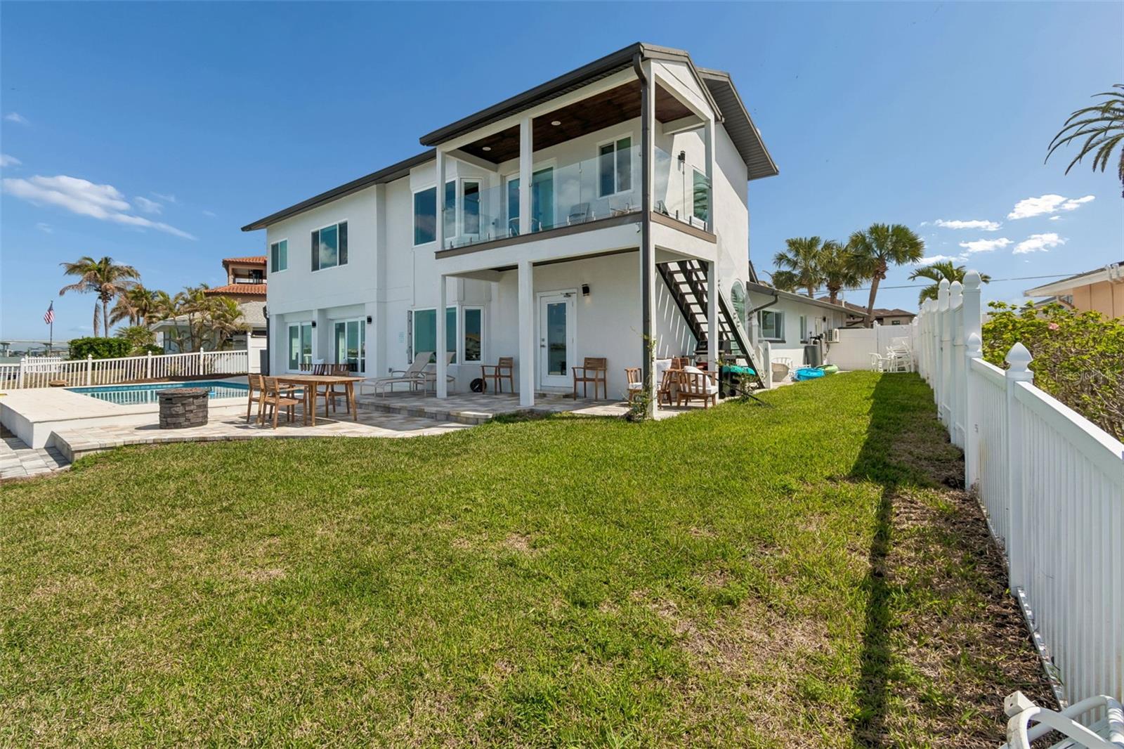 Modern white two-story home with a glass balcony, swimming pool, and fenced grassy yard.