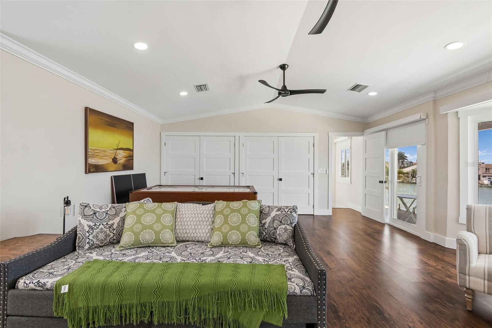 Furnished game room with a pool table behind a patterned sofa and doors overlooking the water.