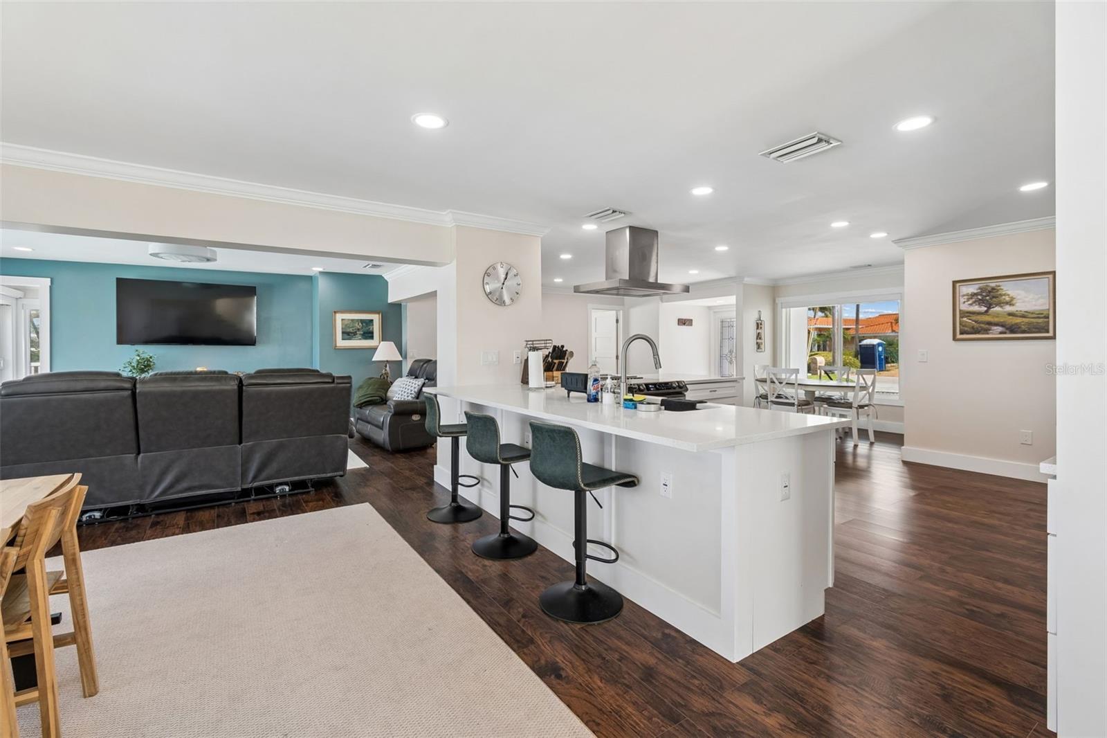 Open-plan kitchen and living room with a white island, teal accent wall, and dark wood floors.