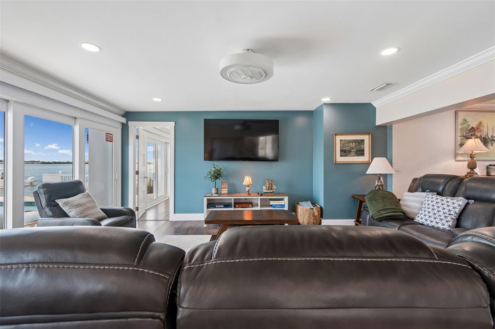Waterfront living room with a blue accent wall, leather sofas, and sliding doors overlooking the water.