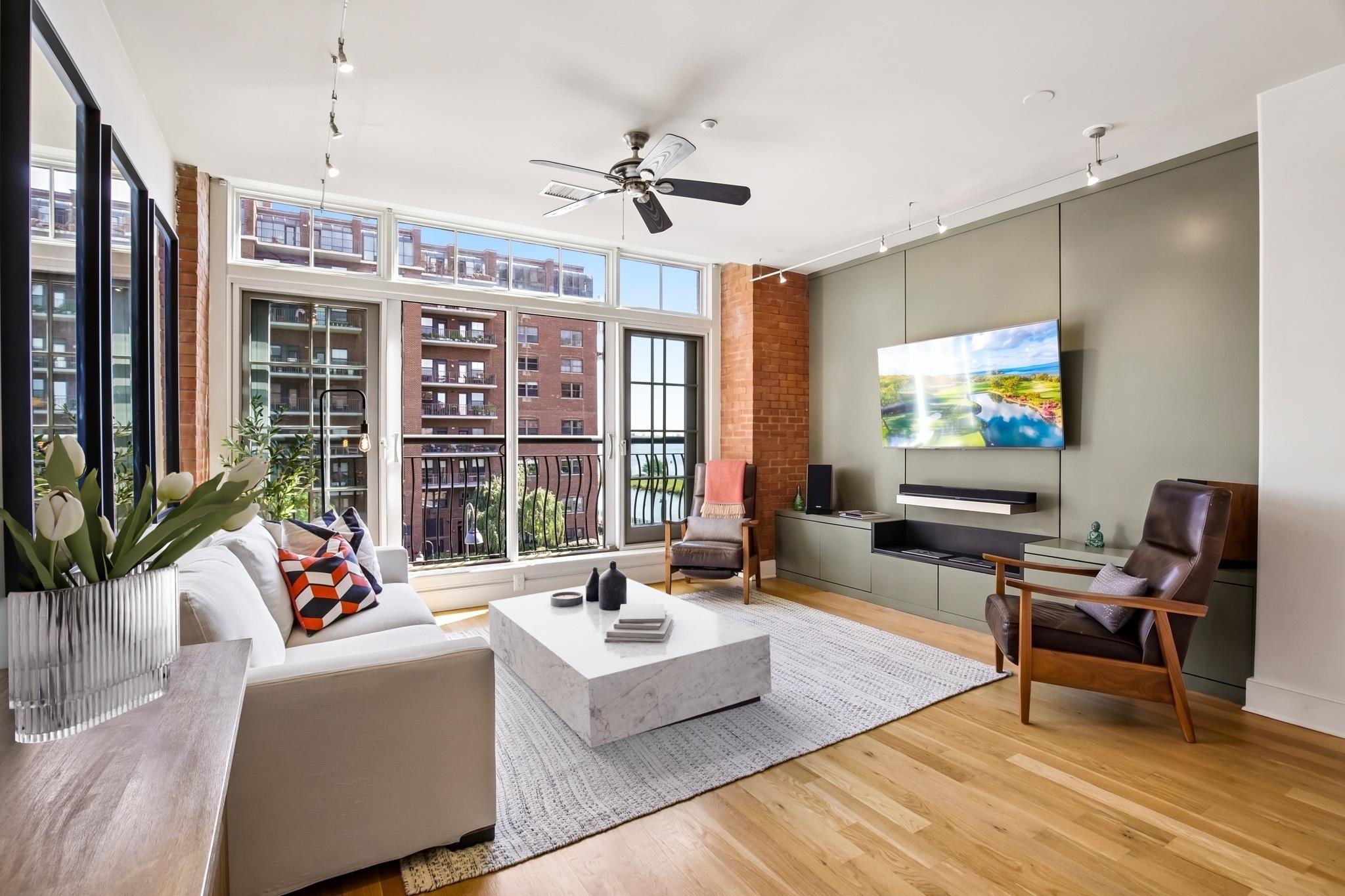 Living room with floor-to-ceiling windows, exposed brick columns, and a balcony with a water view.