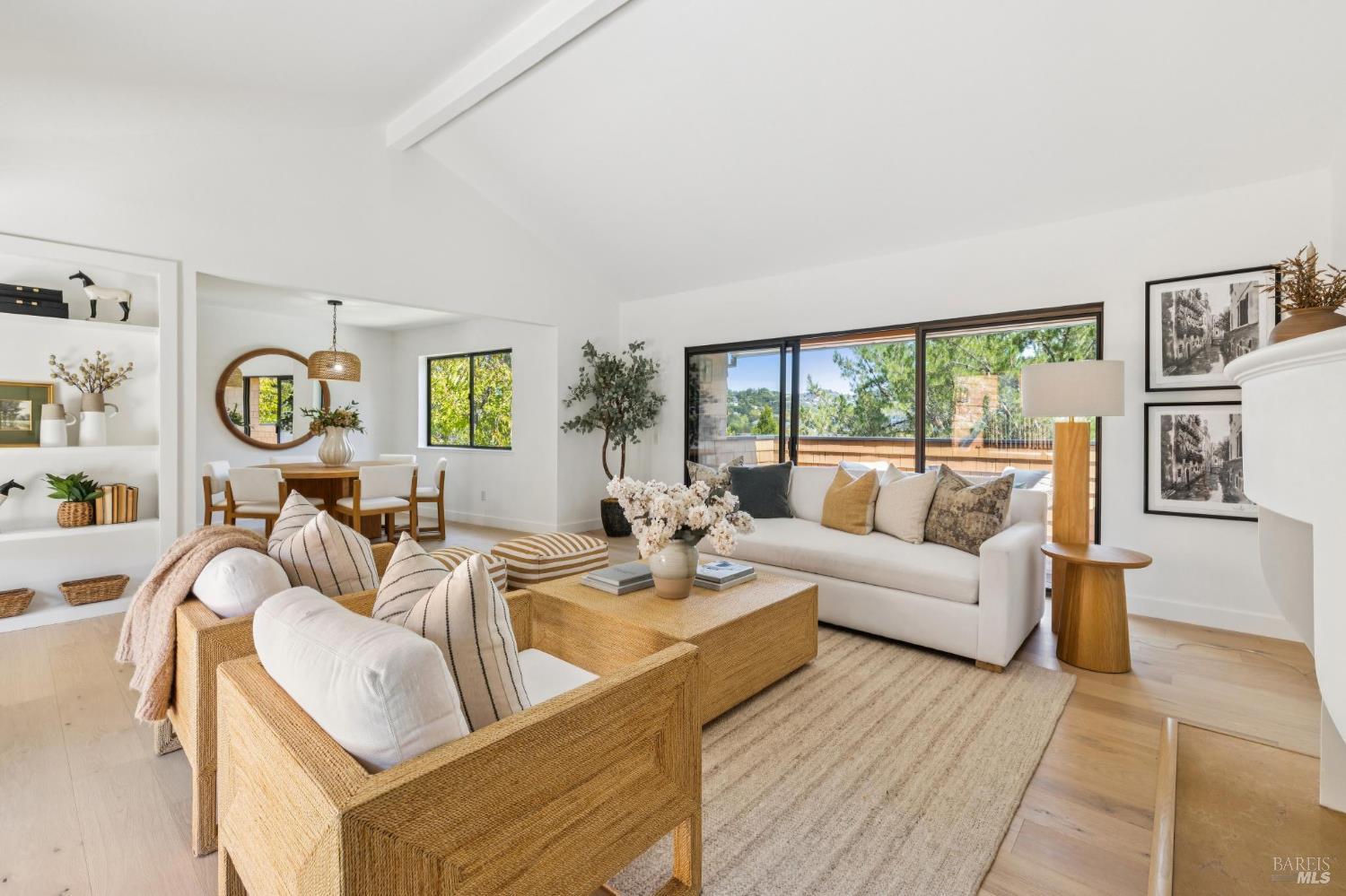 Staged living room with woven seating, adjoining dining area, and wide doors opening to a terrace.