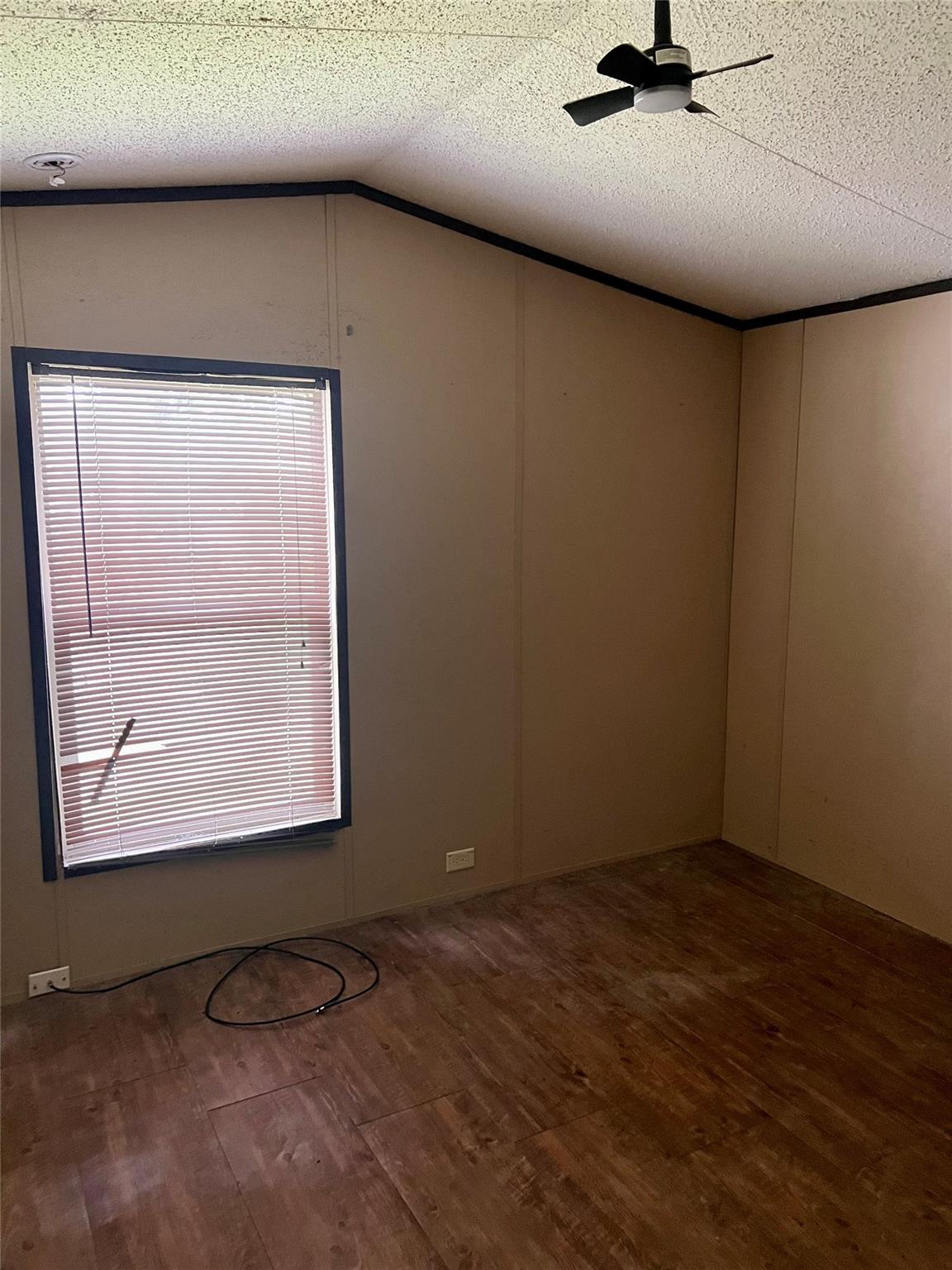Empty room with wood-look flooring, a window with closed blinds, and a ceiling fan.