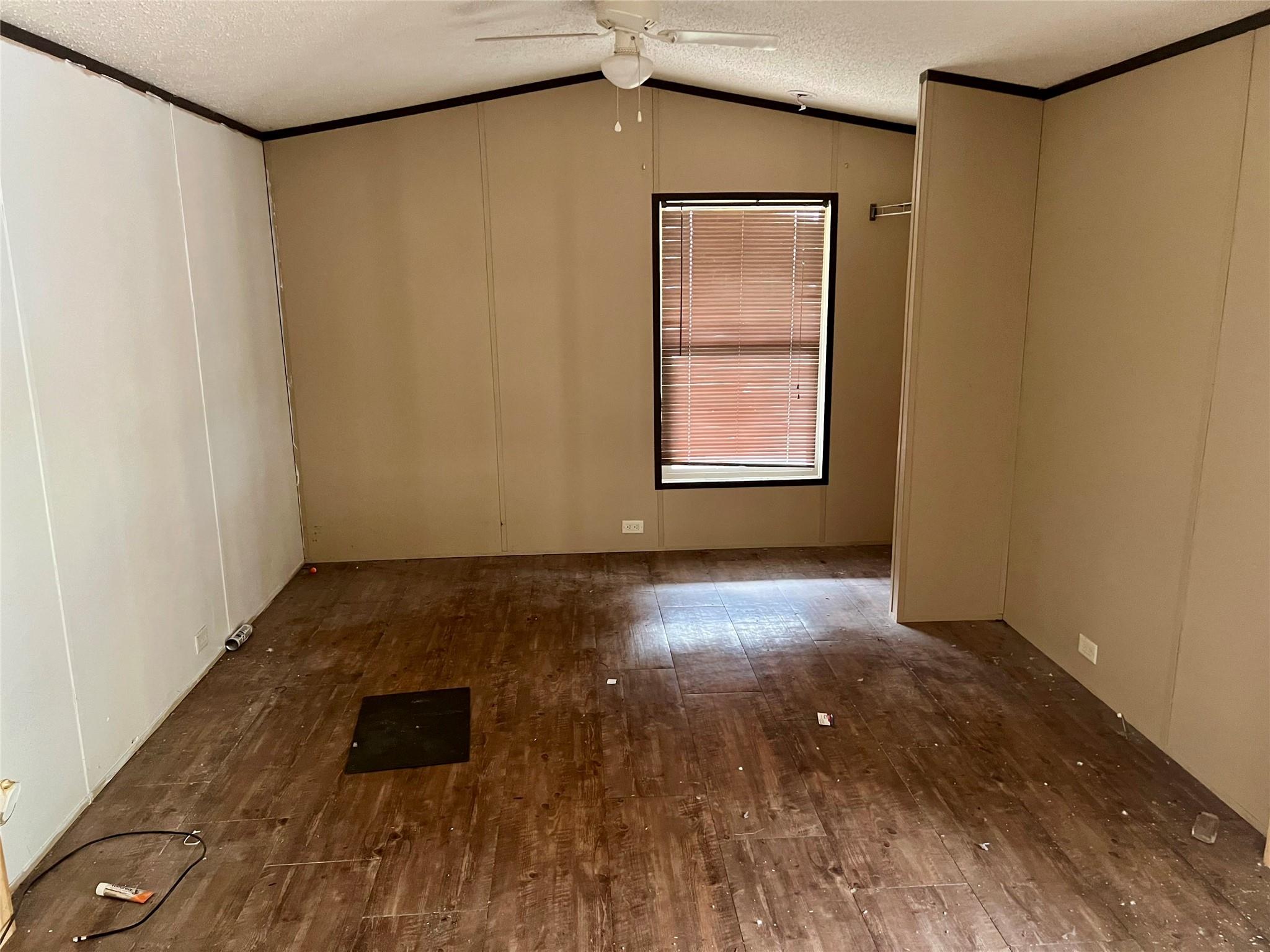 Vacant bedroom with worn wood flooring, a ceiling fan, and a window with closed blinds.