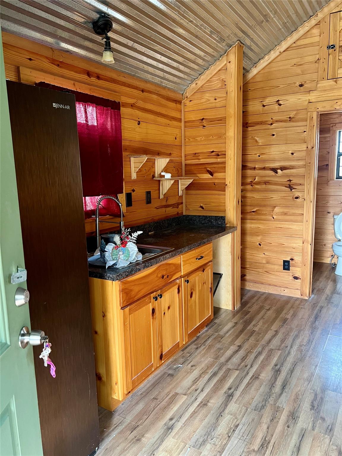 Compact knotty-pine kitchen with a dark countertop, sink, and red window curtain.
