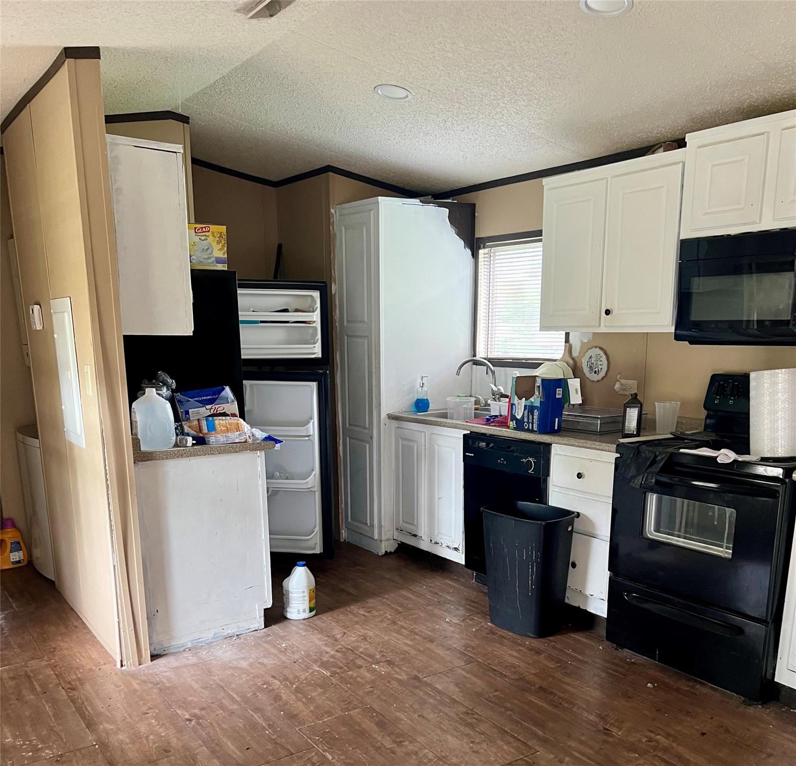 Kitchen with white cabinets, black appliances, an open refrigerator, and cluttered counters.