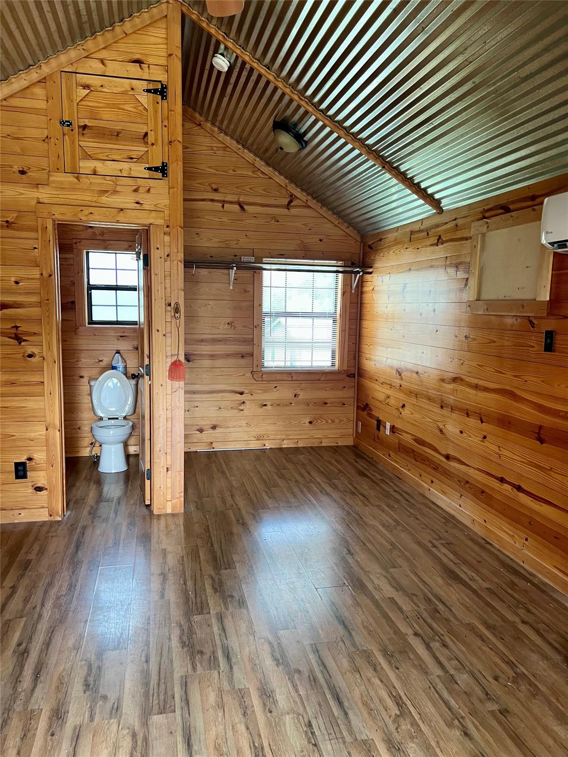 Unfurnished wood-paneled room with a vaulted metal ceiling and bathroom doorway.