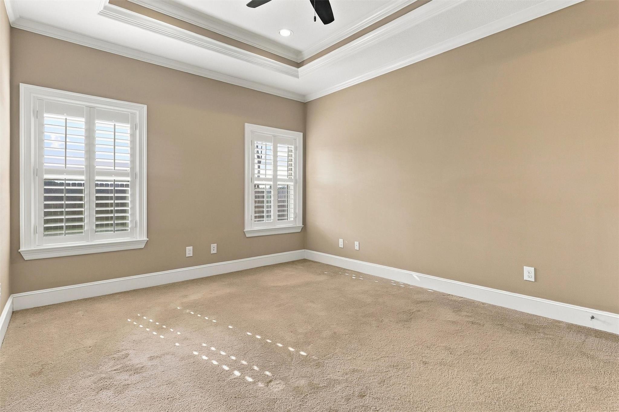 Empty carpeted room with two plantation-shuttered windows and a tray ceiling.