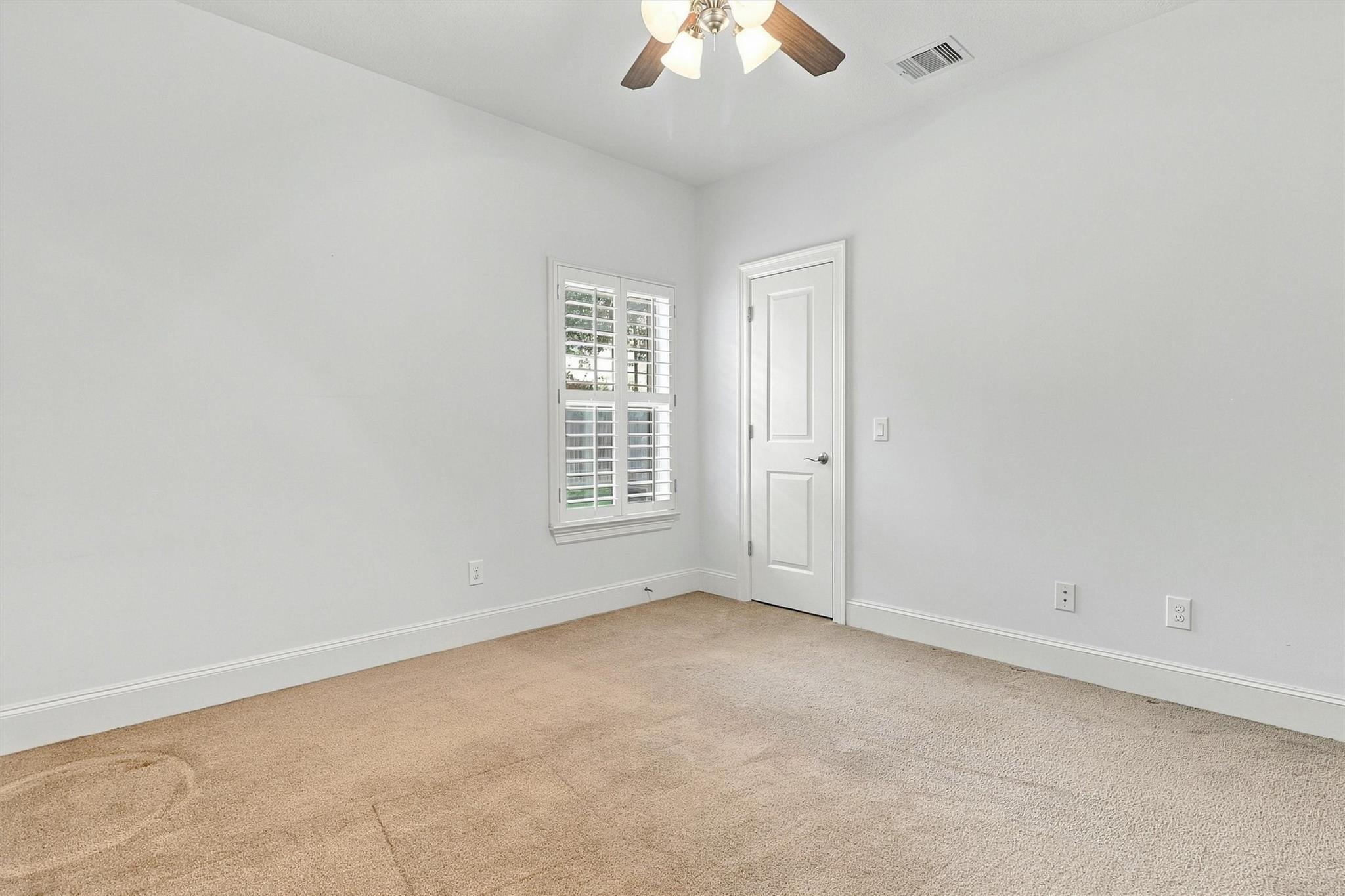 Empty carpeted room with a shuttered window and ceiling fan with lights.