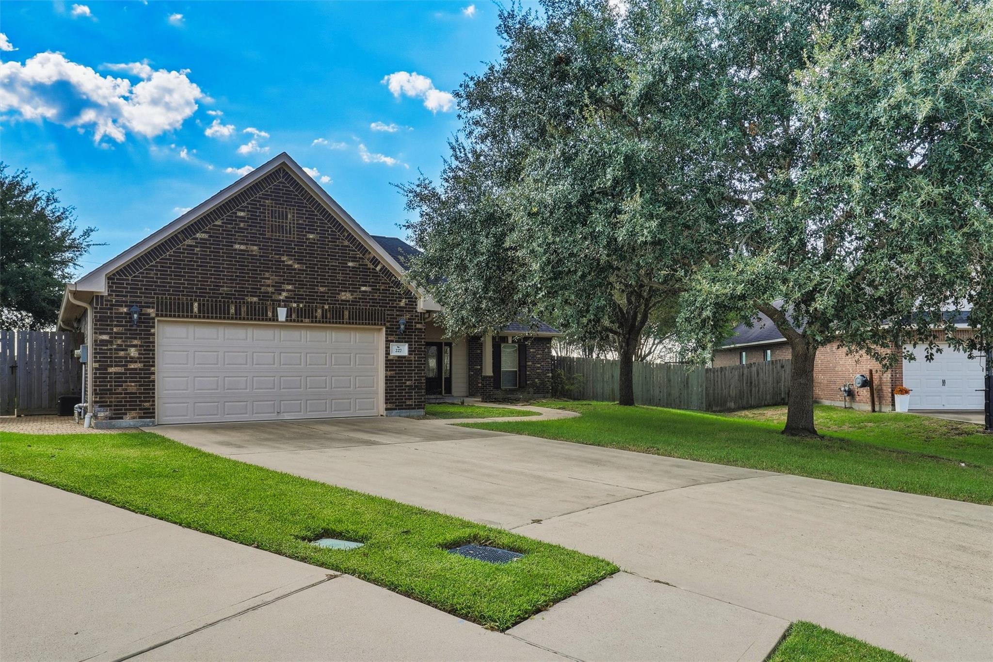 Dark brick house with a double garage, broad driveway, and mature trees shading the front lawn.
