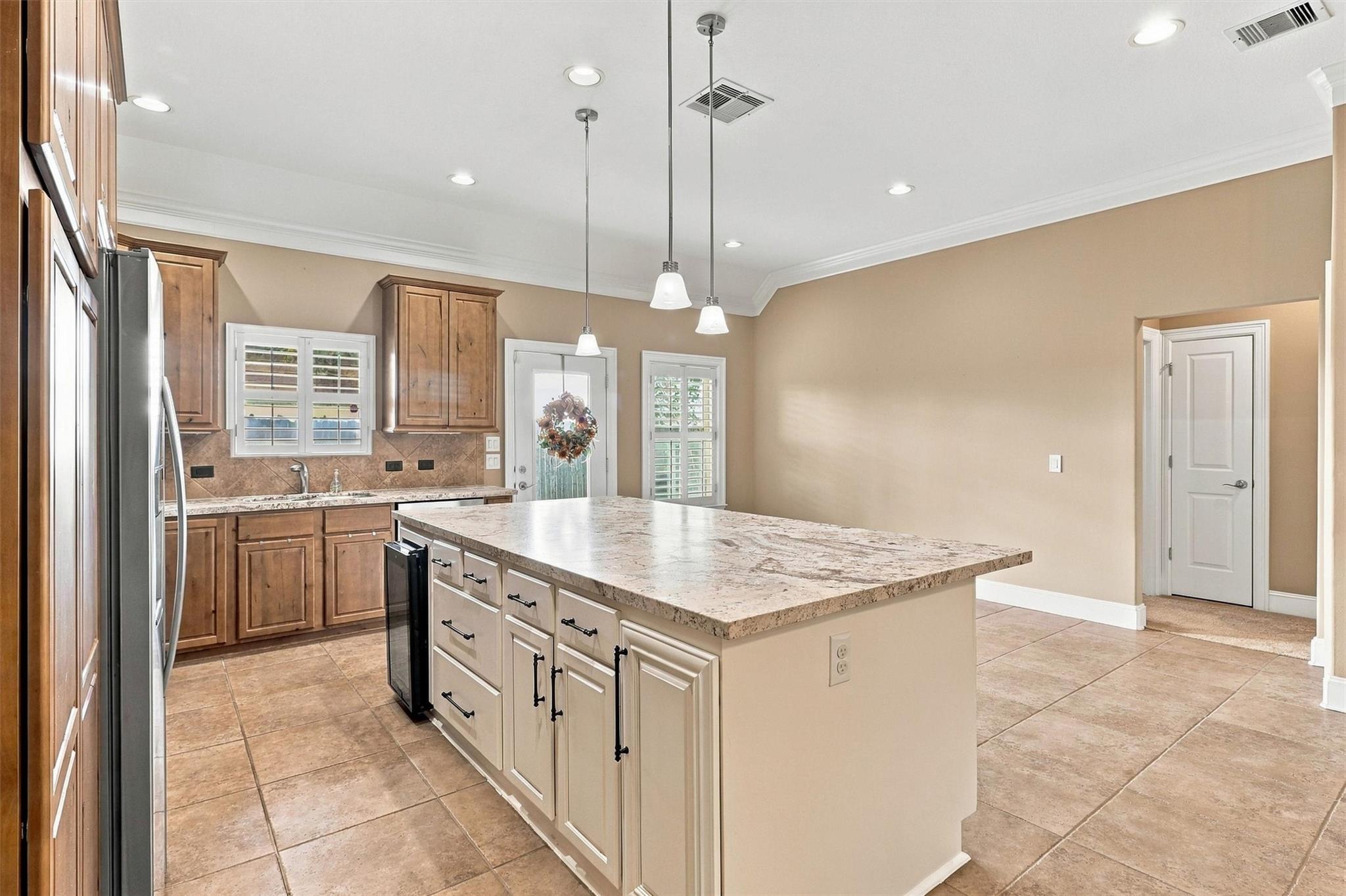 Kitchen with a large granite island, wood cabinetry, stainless steel appliances, and shuttered windows.