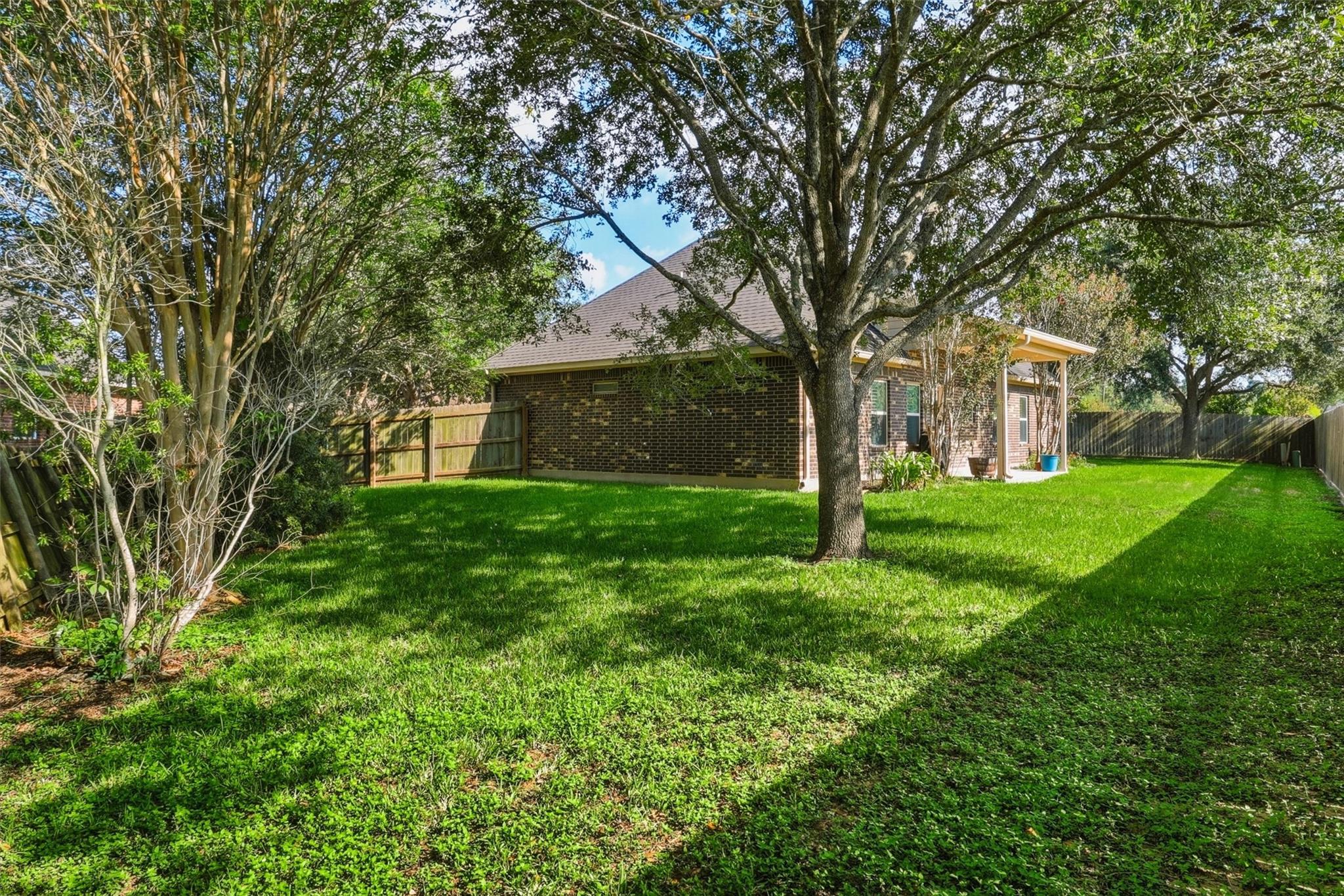 Brick house behind a tree-shaded, fenced lawn, with a covered patio.