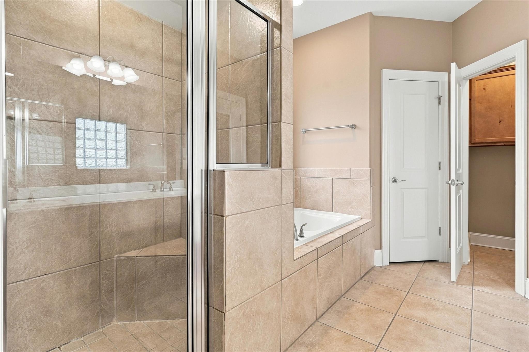 Bathroom with a glass shower, built-in tub, and tan tile throughout.