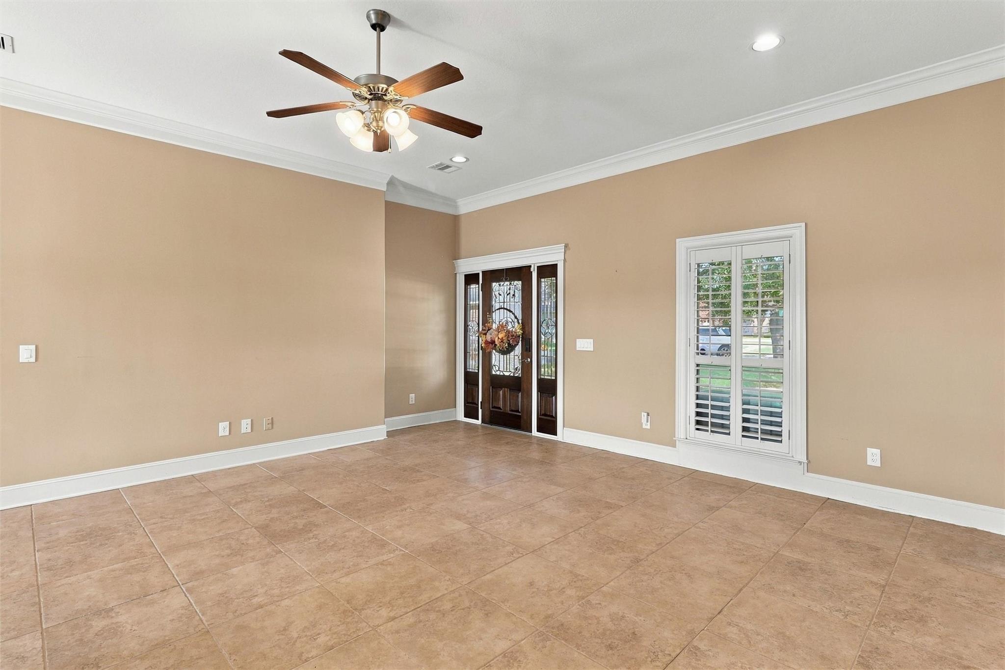 Empty tiled entry room with a decorative glass front door and plantation-shuttered window.