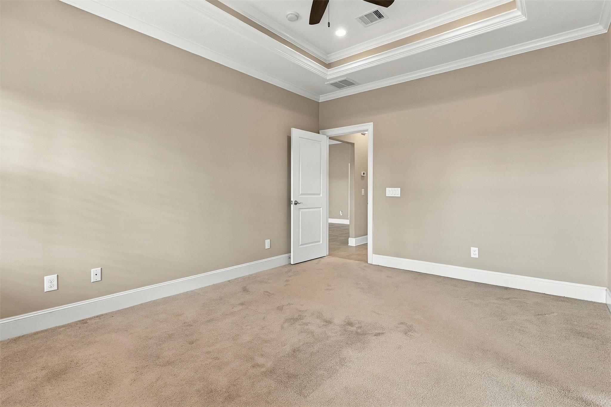 Empty carpeted room with a tray ceiling, ceiling fan, and open door to a tiled area.