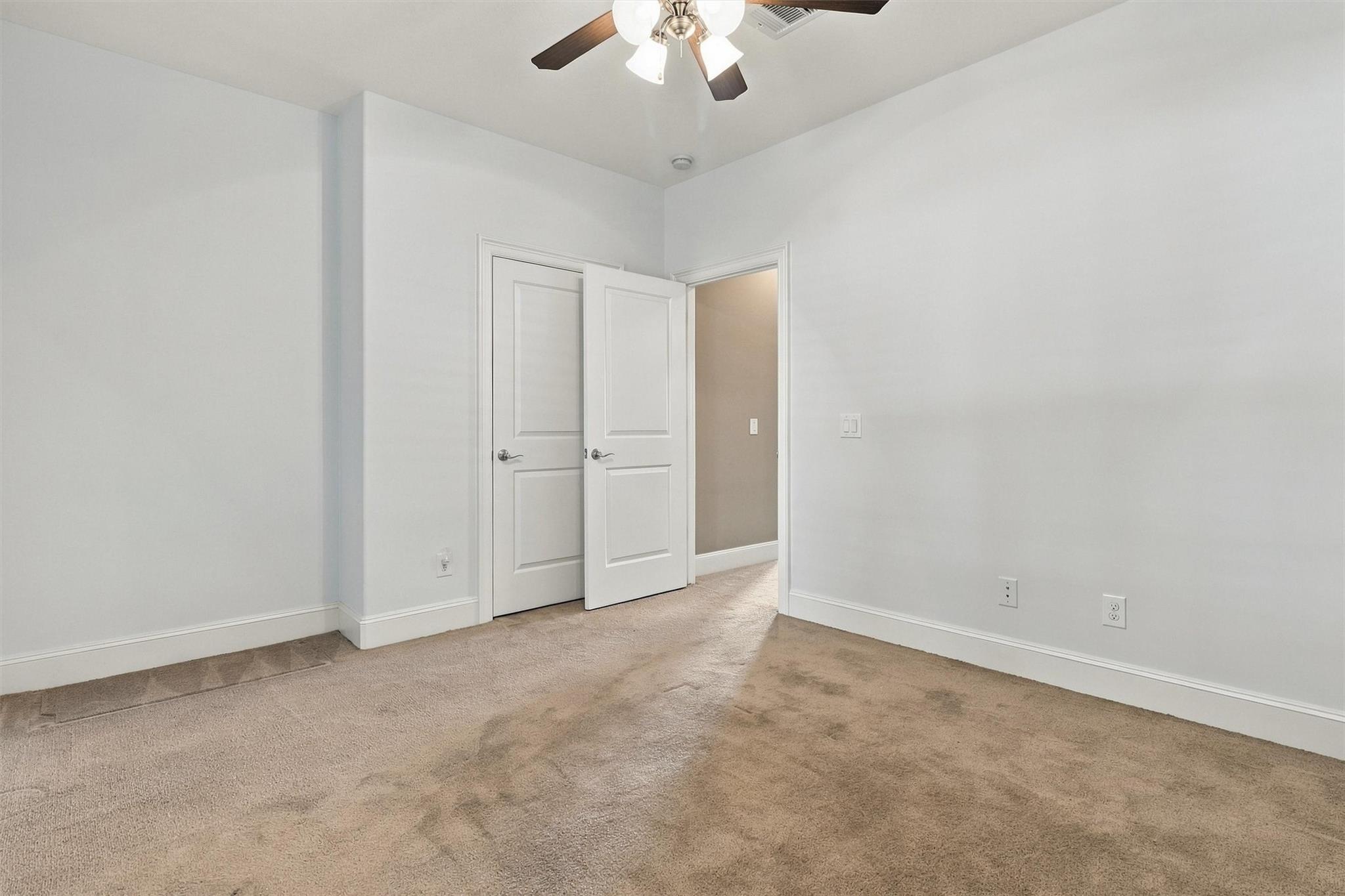 Empty bedroom with beige carpet, a ceiling fan, and open doors.
