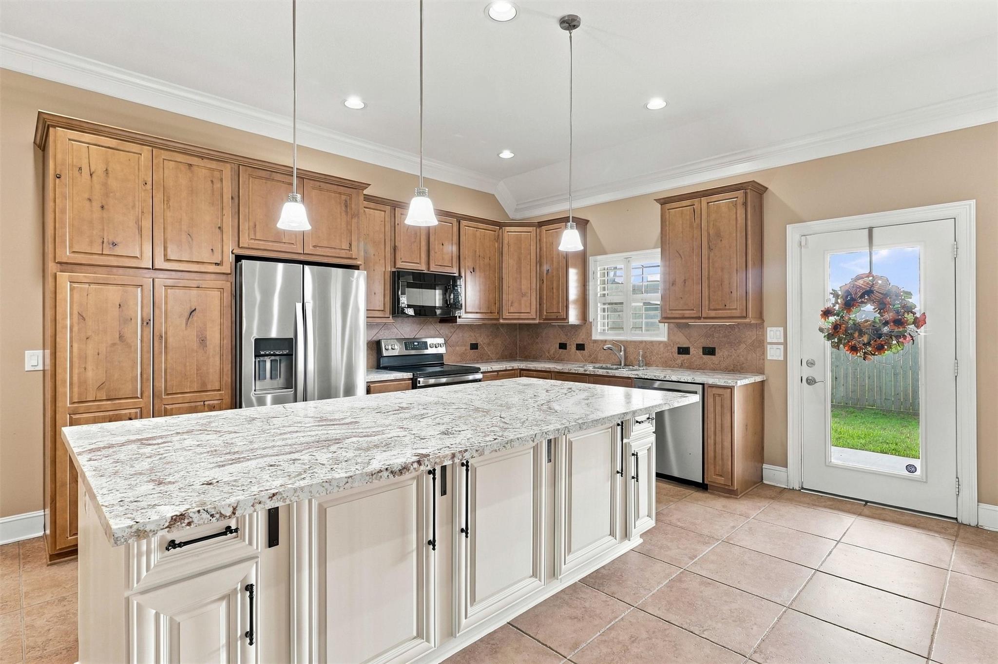 Kitchen with a large granite island, wood cabinets, stainless steel appliances, and a glass back door.