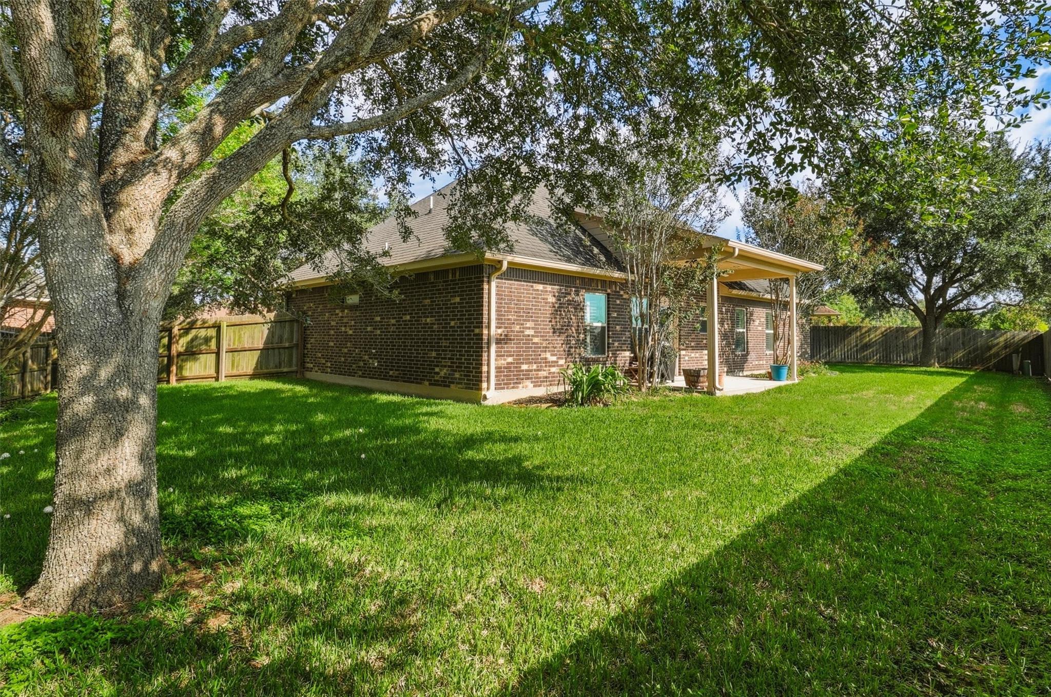 Brick house and covered patio behind a broad lawn shaded by mature trees.