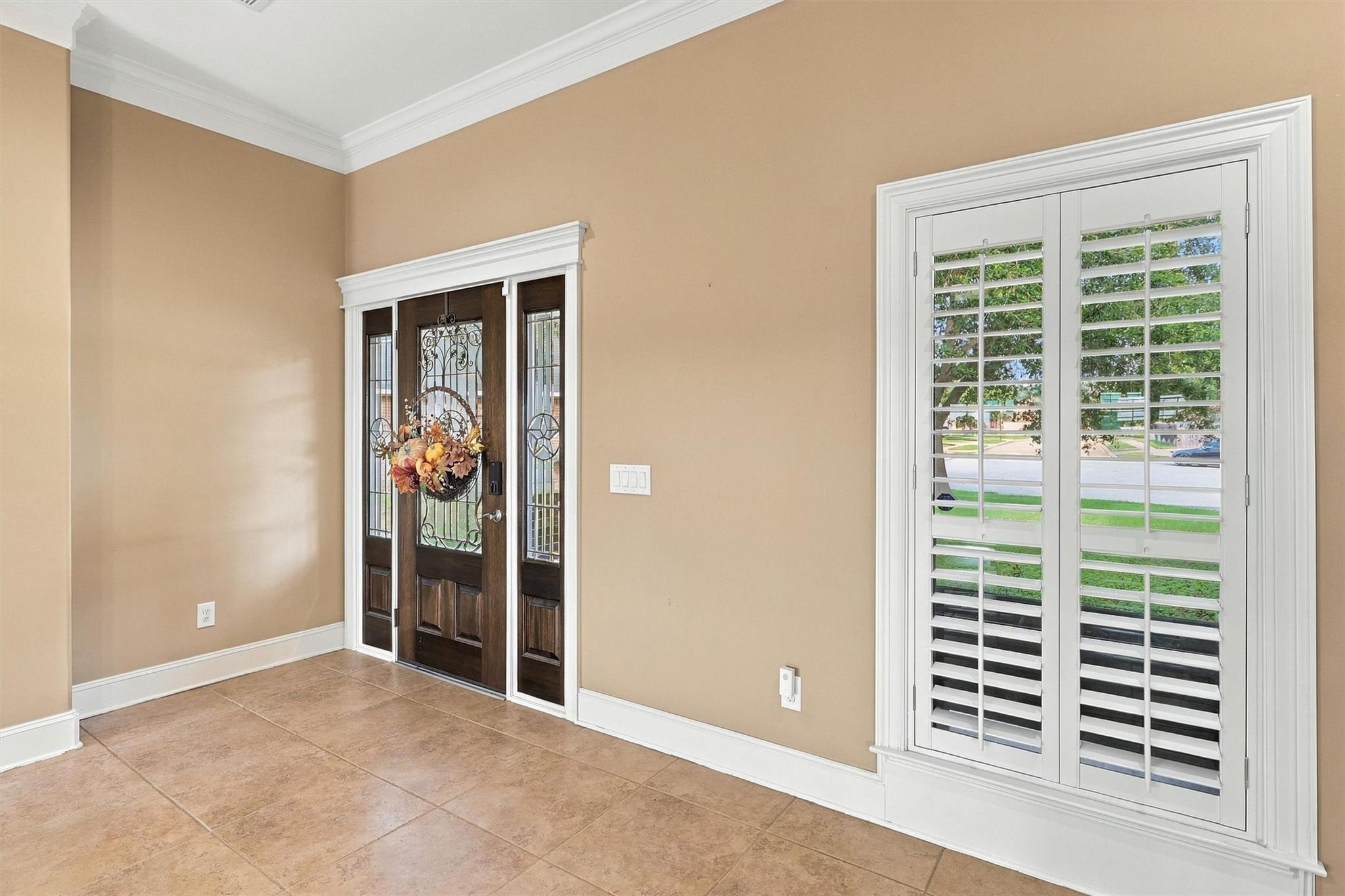 Entry foyer with a dark wood glass-panel front door, tiled floor, and white plantation shutters.