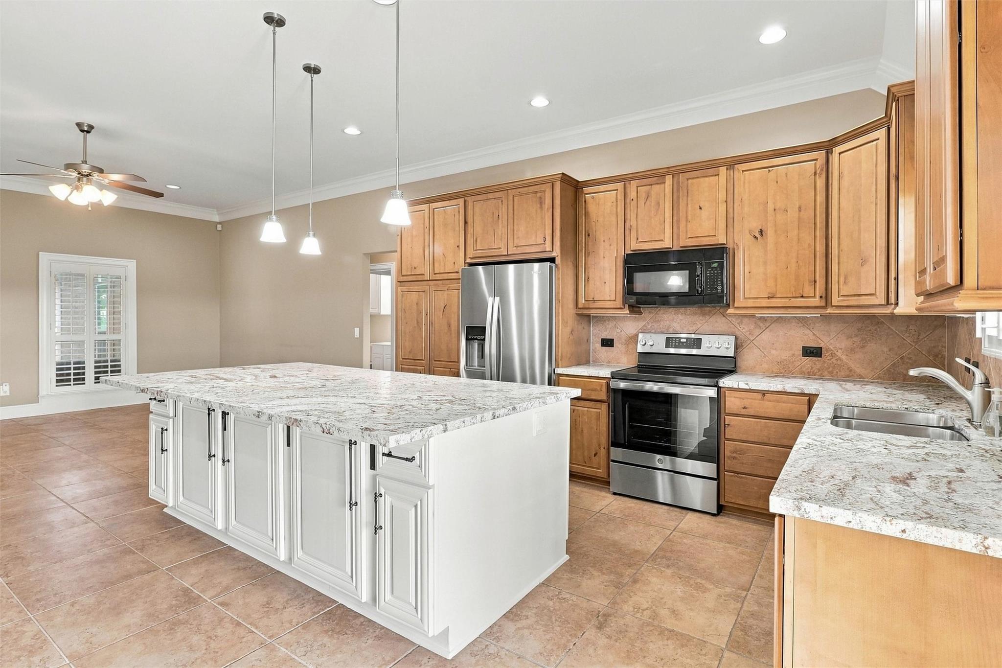 Spacious kitchen with a large white island, warm wood cabinets, and stainless steel appliances.