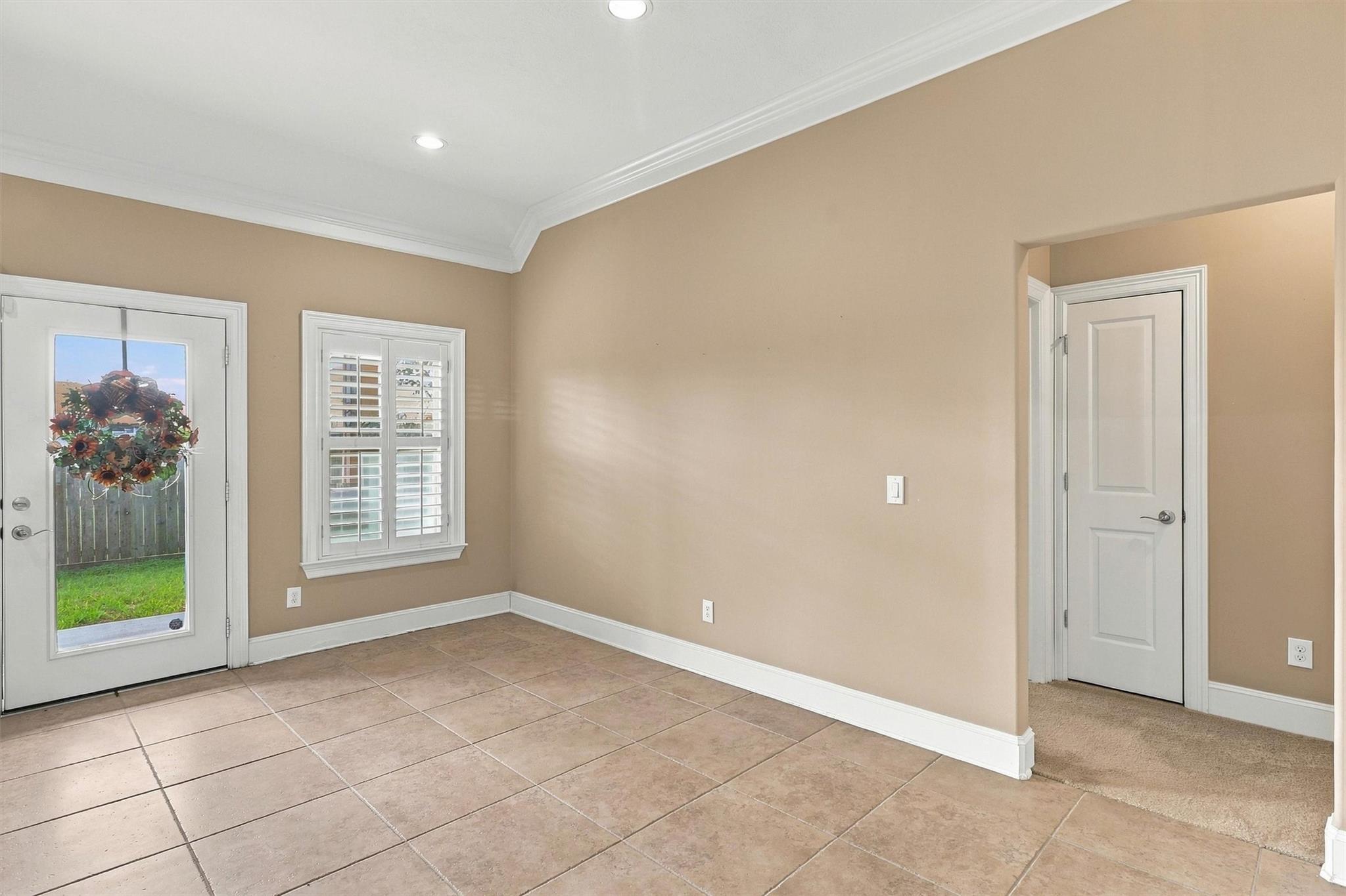 Vacant entry room with tan tile floors, a glass door with a wreath, and a shuttered window.