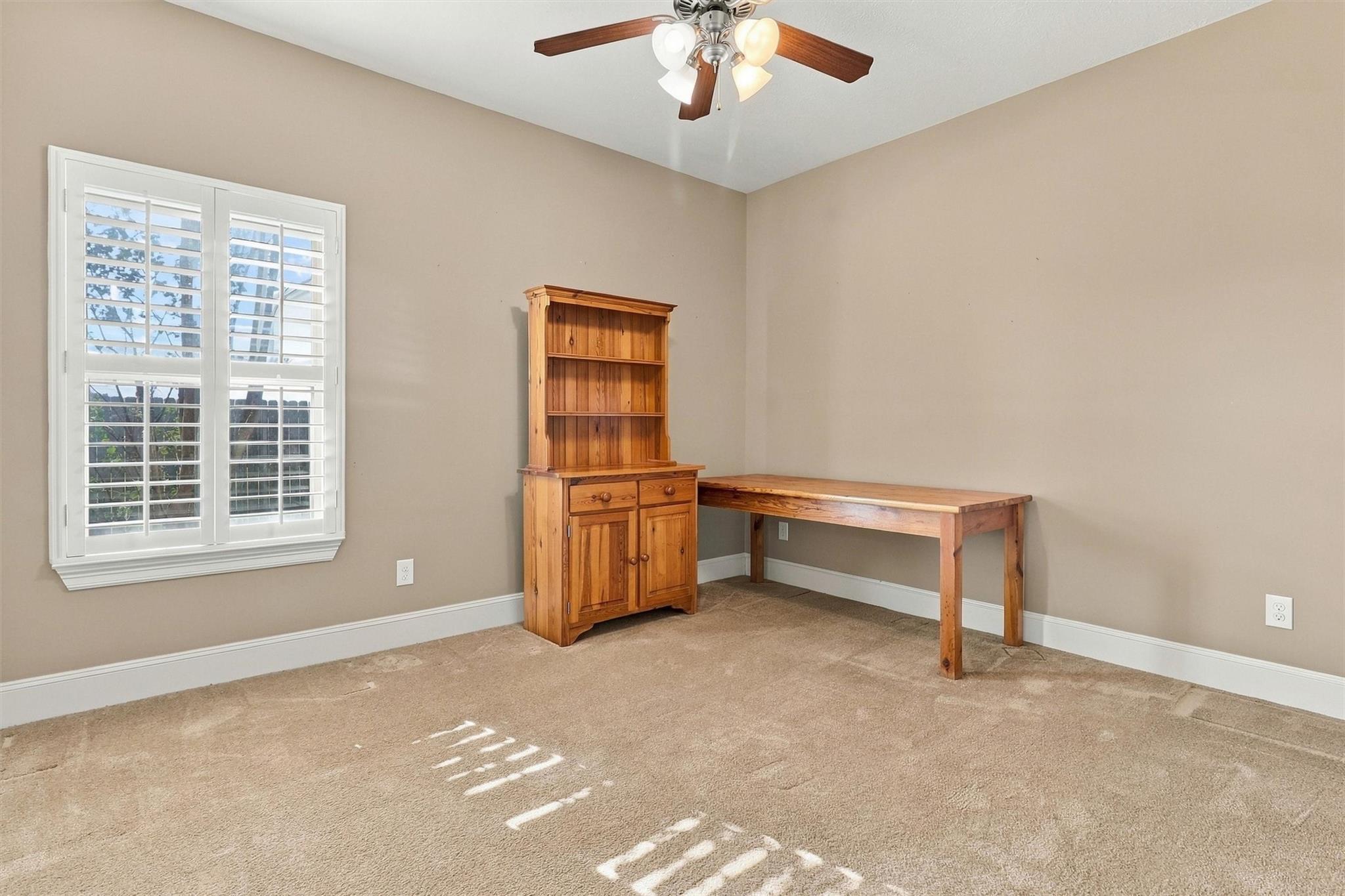 Home office with a wooden desk and hutch beside a plantation-shuttered window.