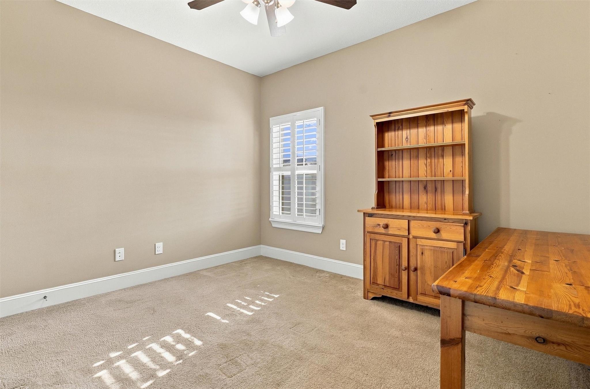 Dining room with a wooden table and hutch beside a shuttered window.